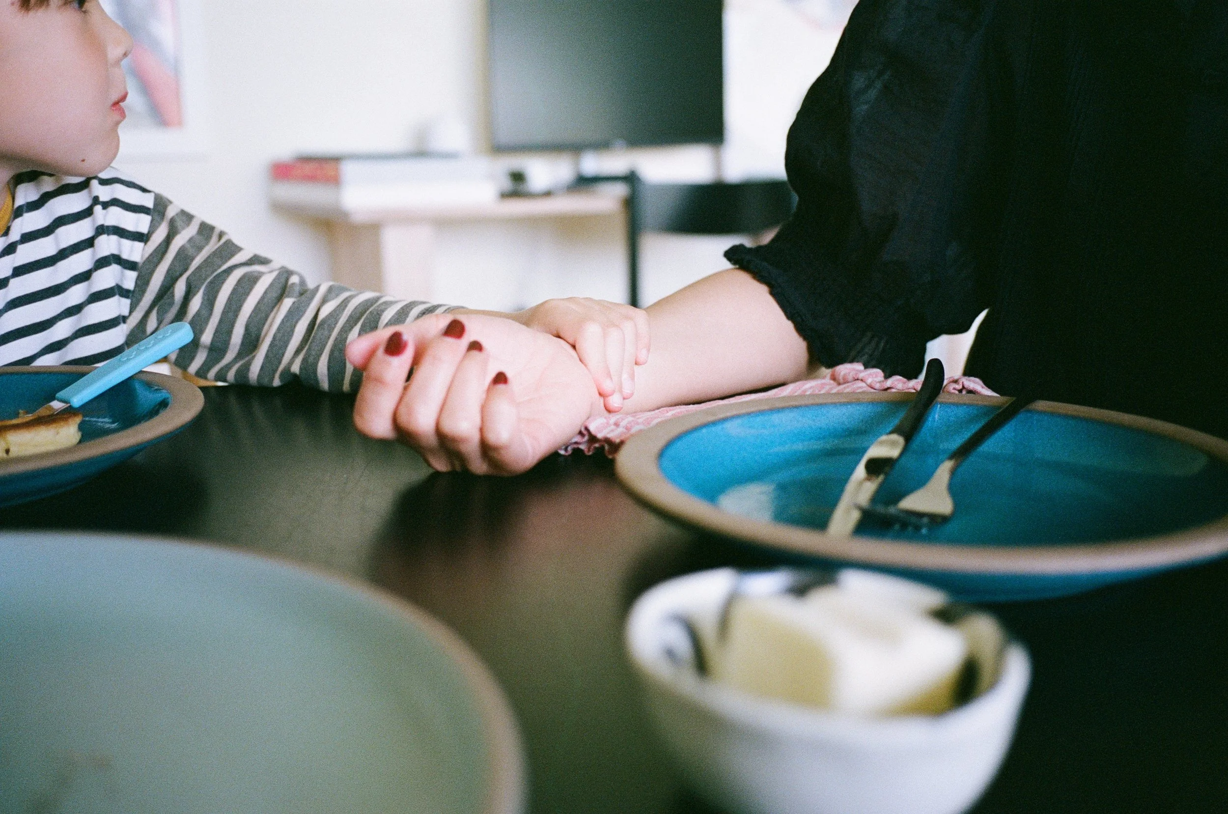 a color 35mm film photo of a little boy sitting at a dining table in their home in Sausalito, California eating pancakes. The little boy has his hand on his mother's arm. 