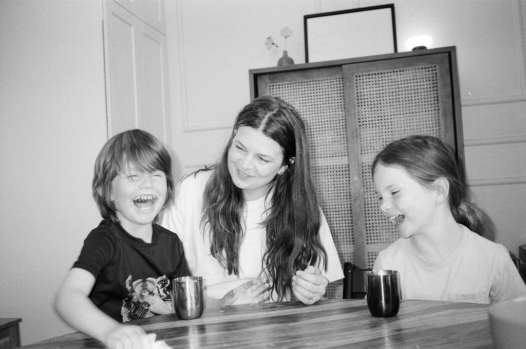 A woman with two children smiling and laughing at a table.