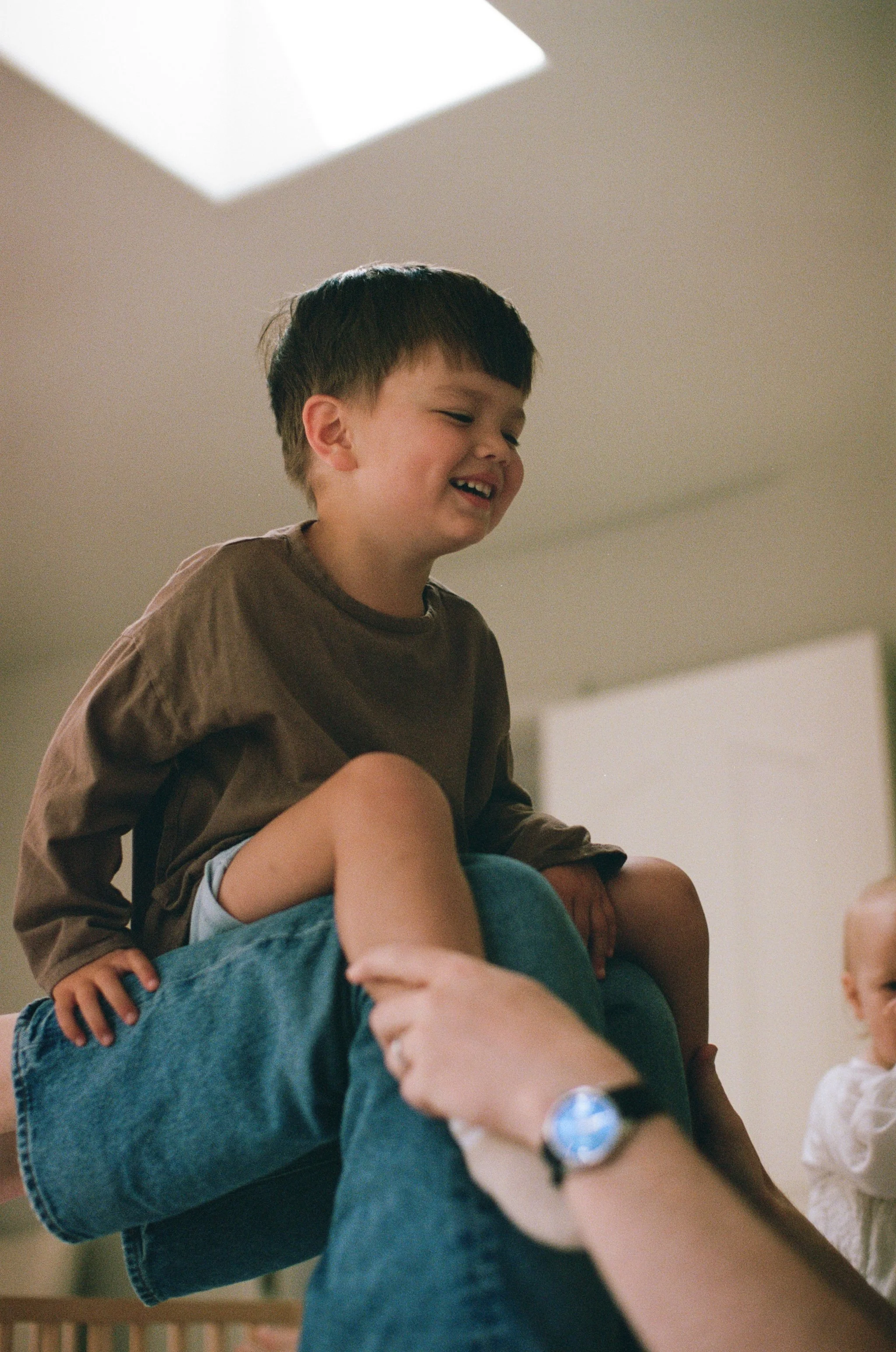 a color 35mm film photo of a little boy sitting on his fathers shins while they play on the bed in their home in Sausalito, California 