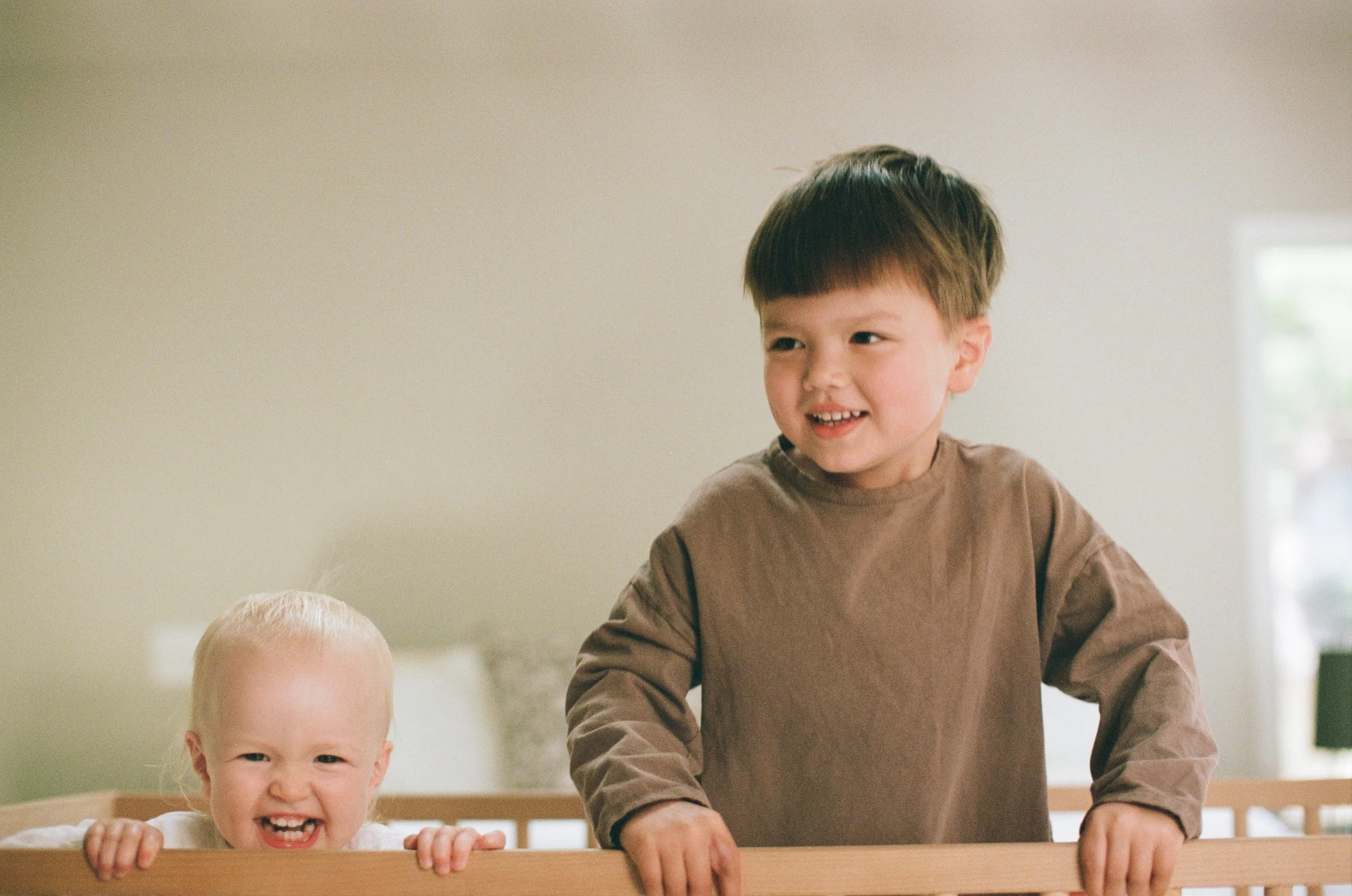 a color 35mm film photo of a little boy and his little sister jumping together in a crib in a bedroom at their home in Sausalito, California 