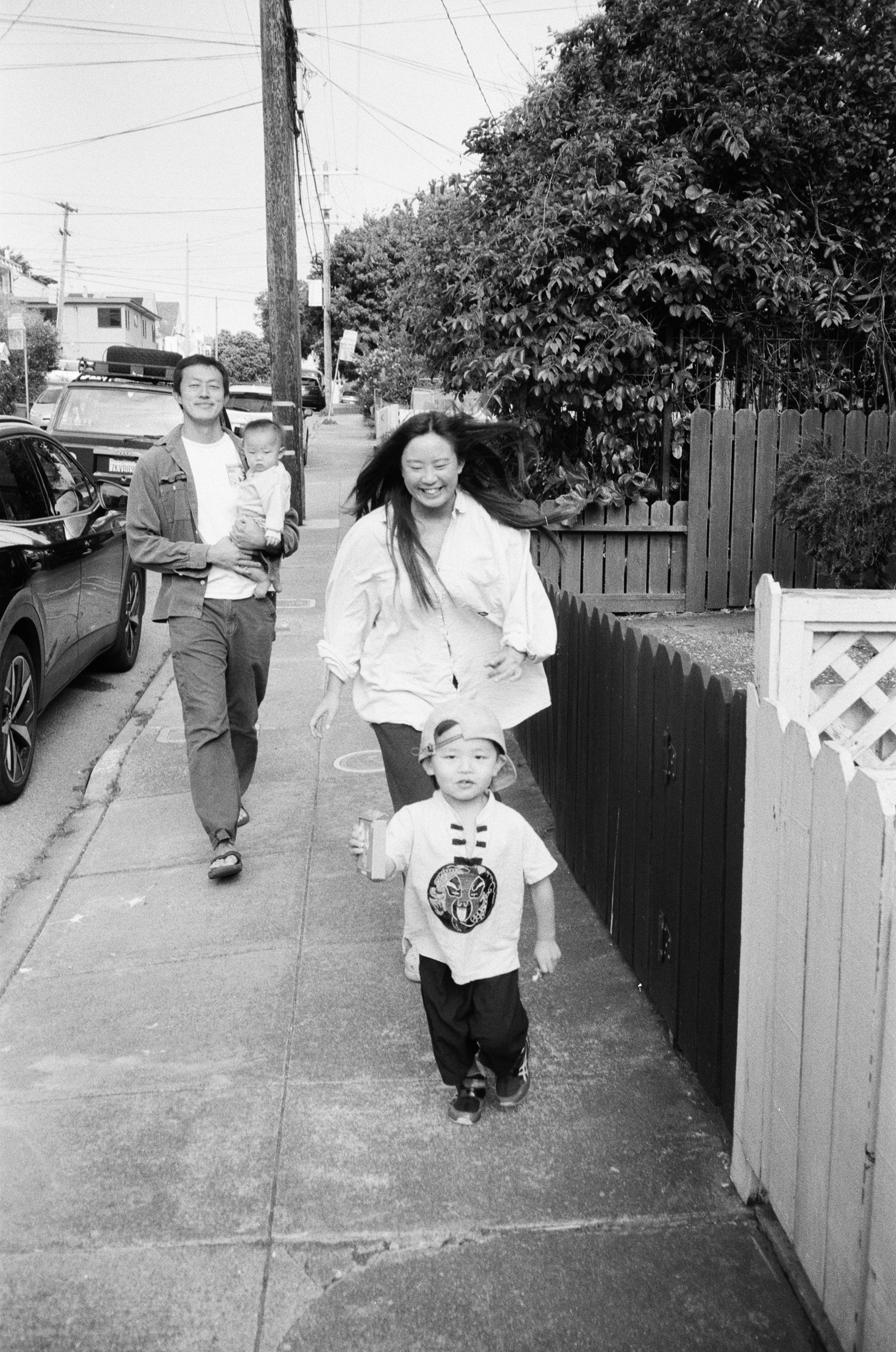 35mm film photo of an Asian family, a mother, father, and two little boys walking down the street. The mother is chasing after the oldest boy. This photo was taken in San Francisco. 