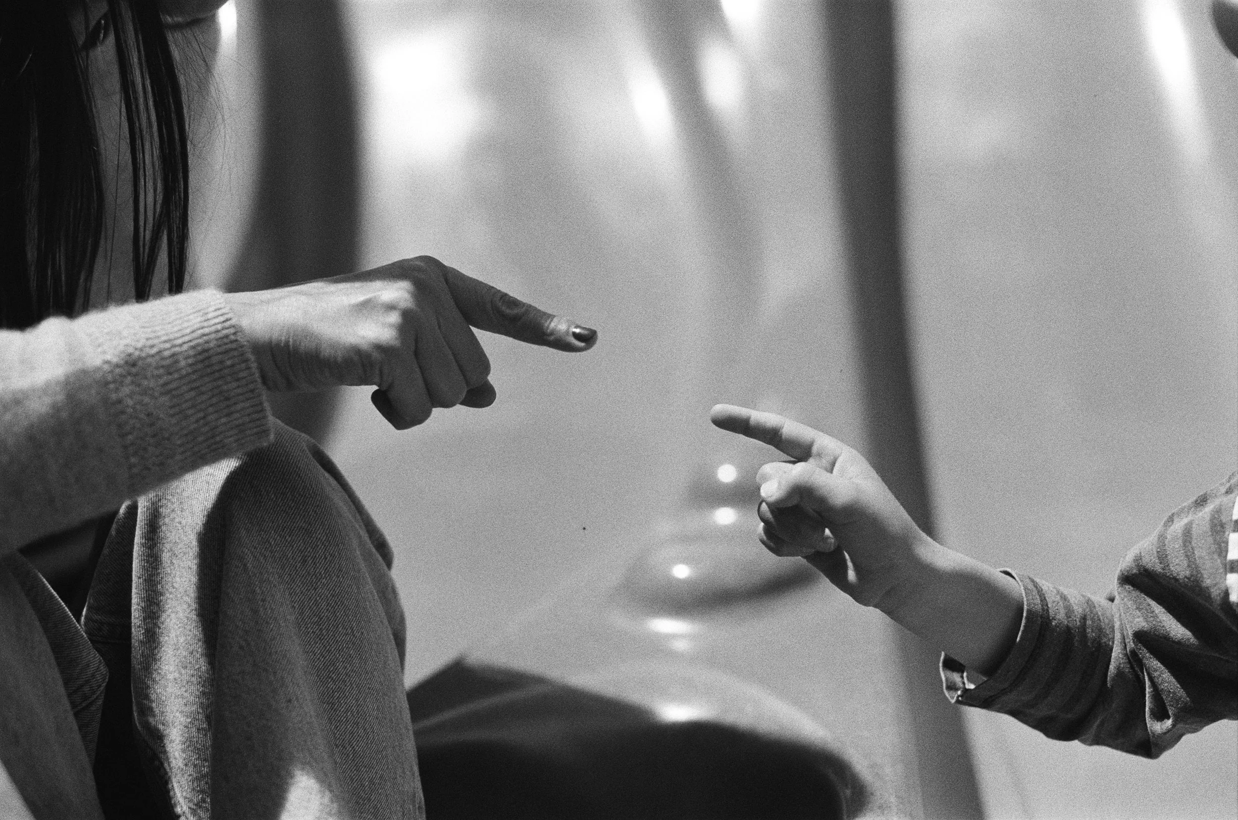35mm black and white photo of a mother and a son touching pointer fingers at the playground. It's a close up of just their fingers. 