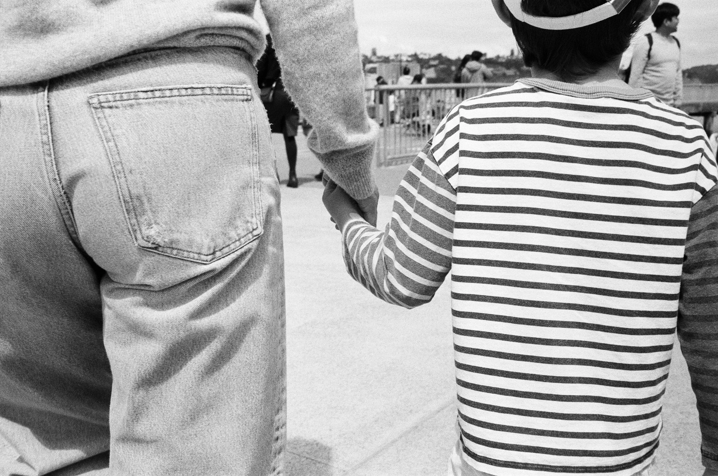 a black and white 35mm film photo of a close up of a mother and son walking and holding hands in Sausalito, California 