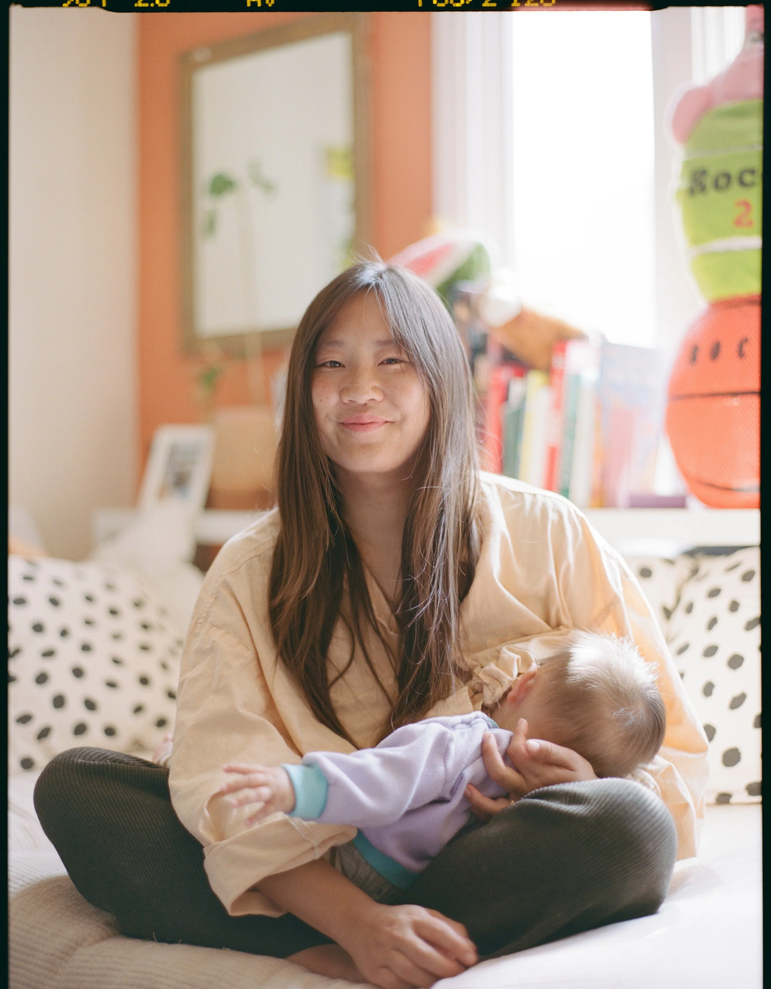 color medium format film image of an asian woman sitting on her couch nursing her infant son in San Francisco, California. 
