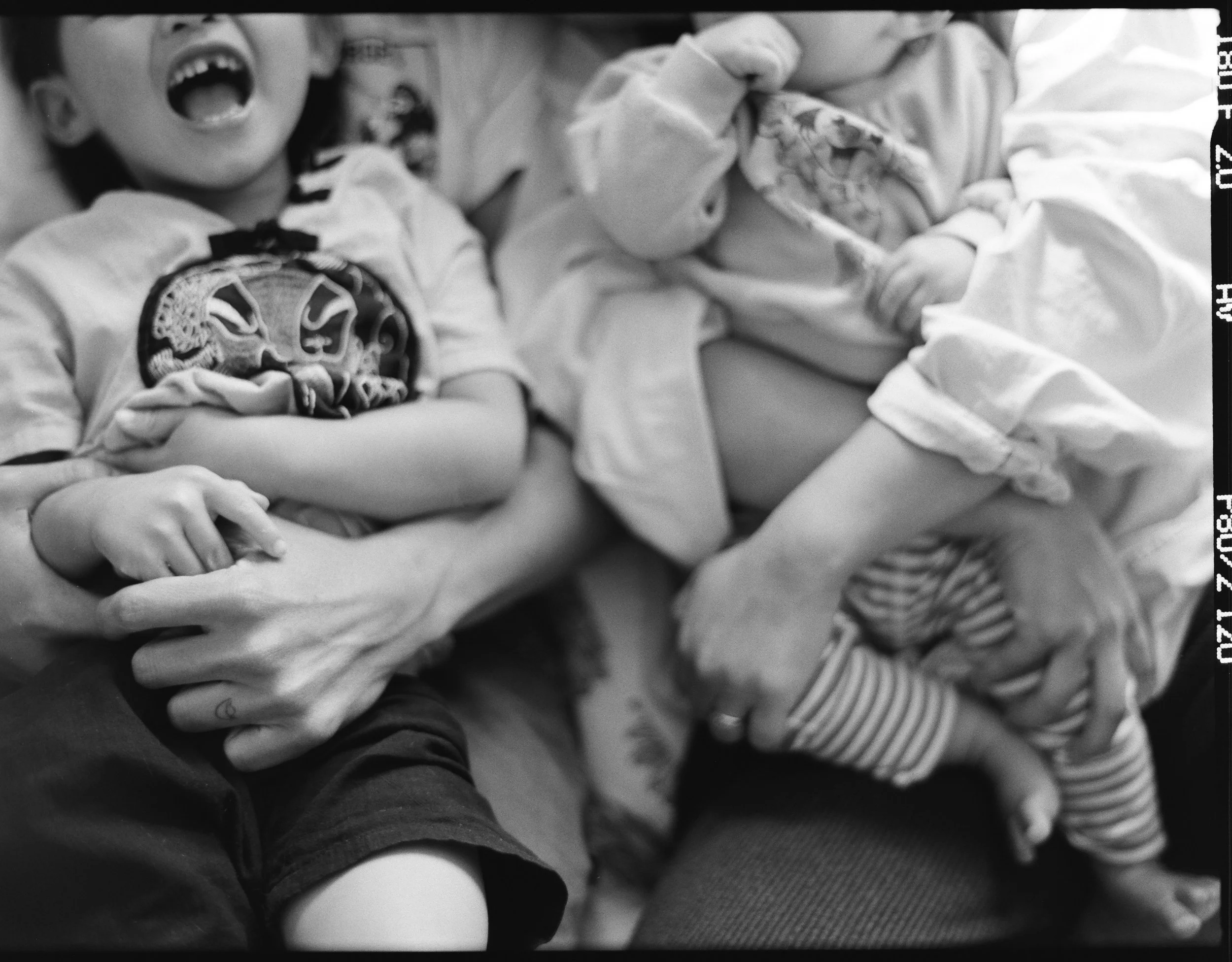 a black and white medium format photo of a family on the couch laughing. The photo is a close up shot of just their hands and arms holding each other. This was taken in their home in San Francisco, California. 