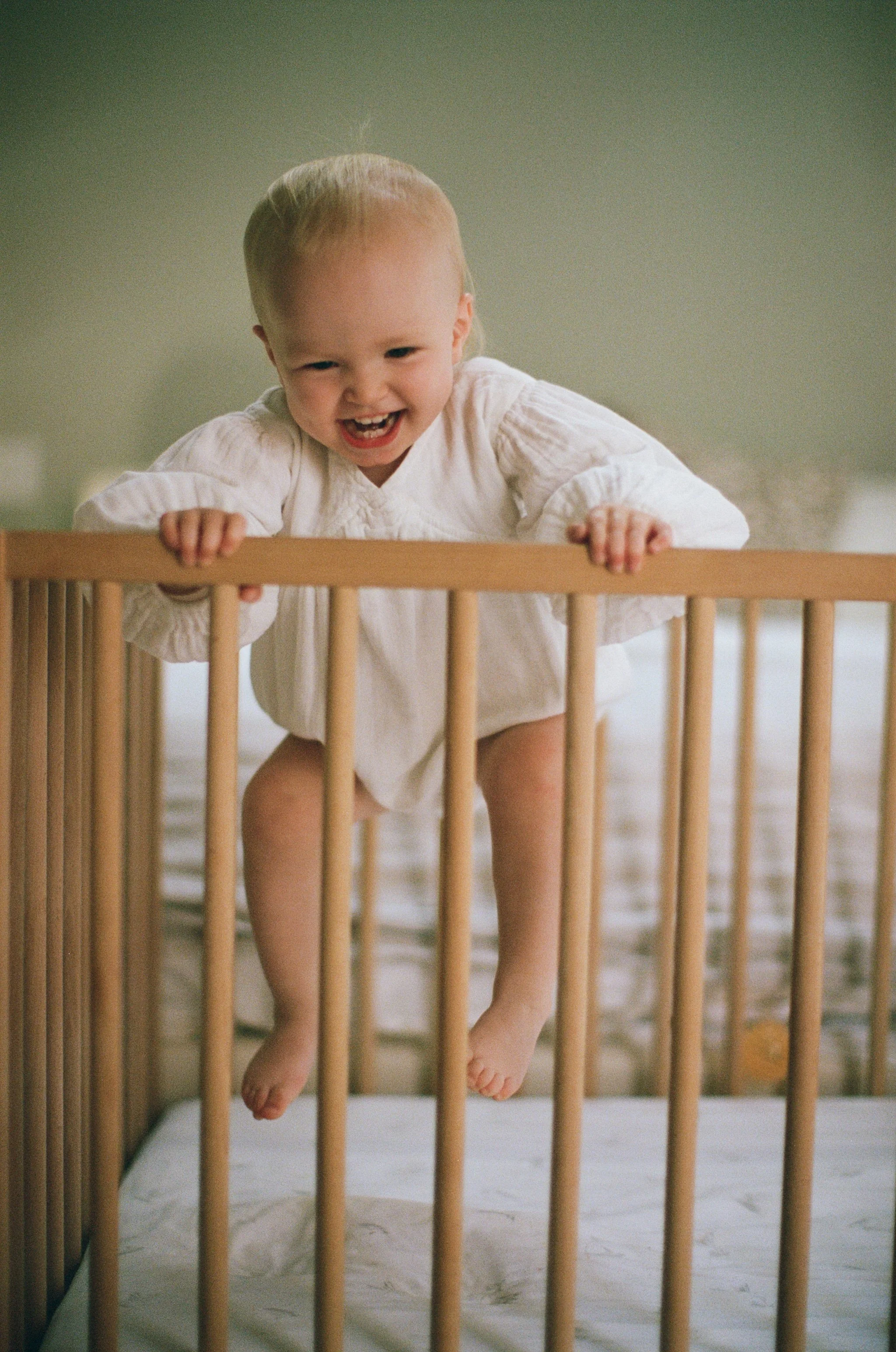 a color 35mm film photo of a little girl who looks to be about 2 years old jumping in her crib with a smile on her face at home in Sausalito, California 