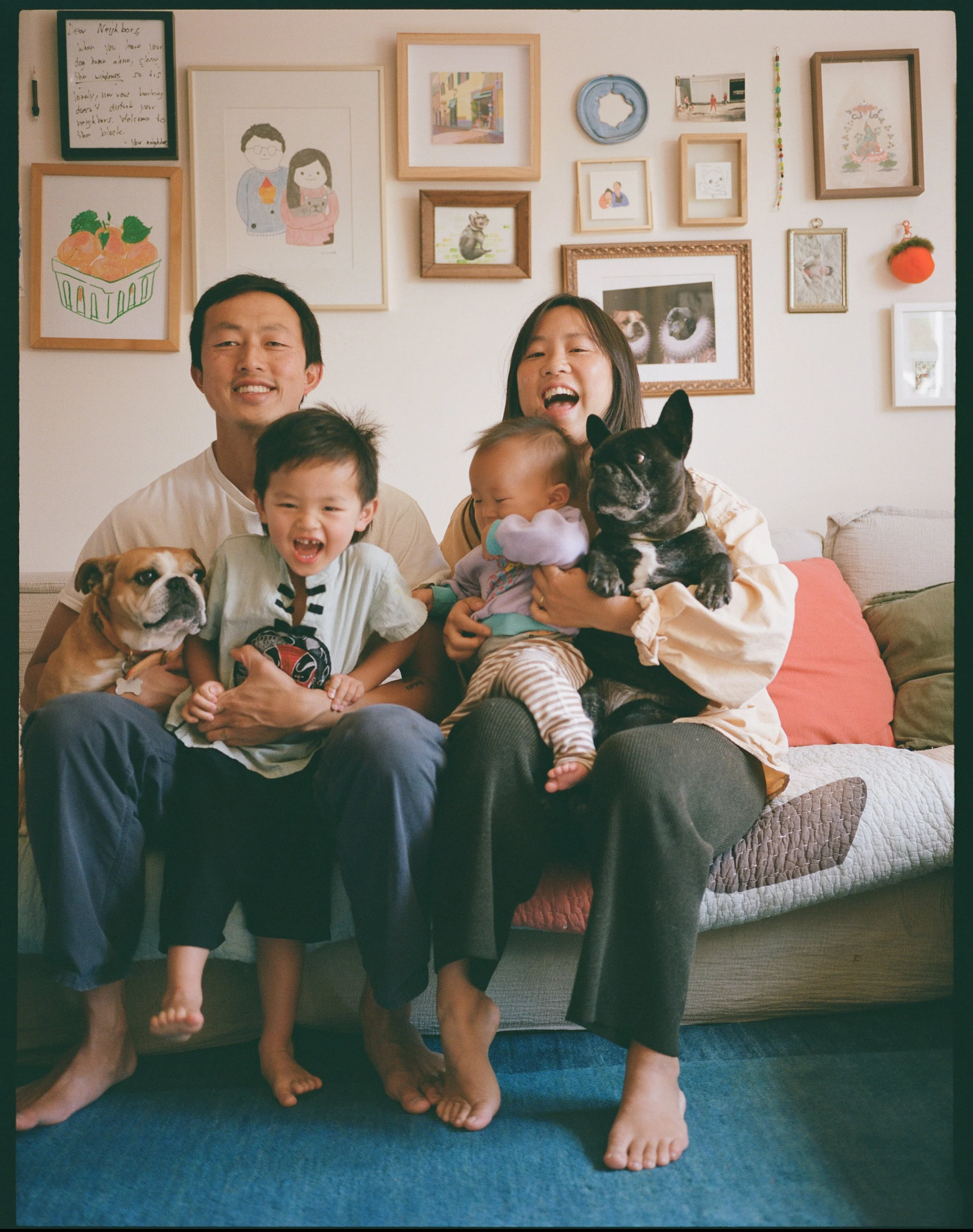 family of 4 sits on their couch and smiles at the camera with their two dogs at their home in san francisco