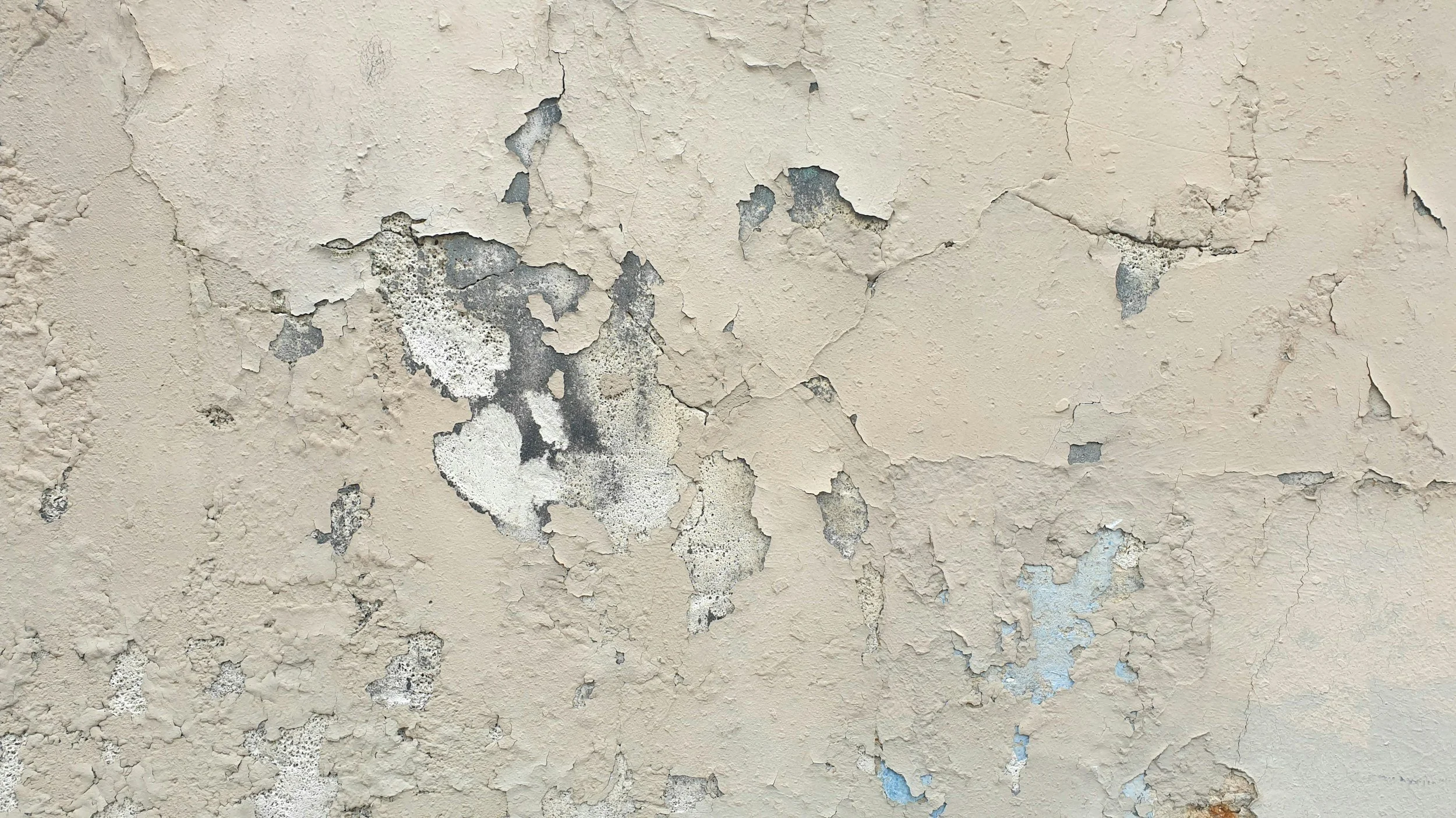 A close-up of a beige wall with peeling paint and exposed underneath layers.