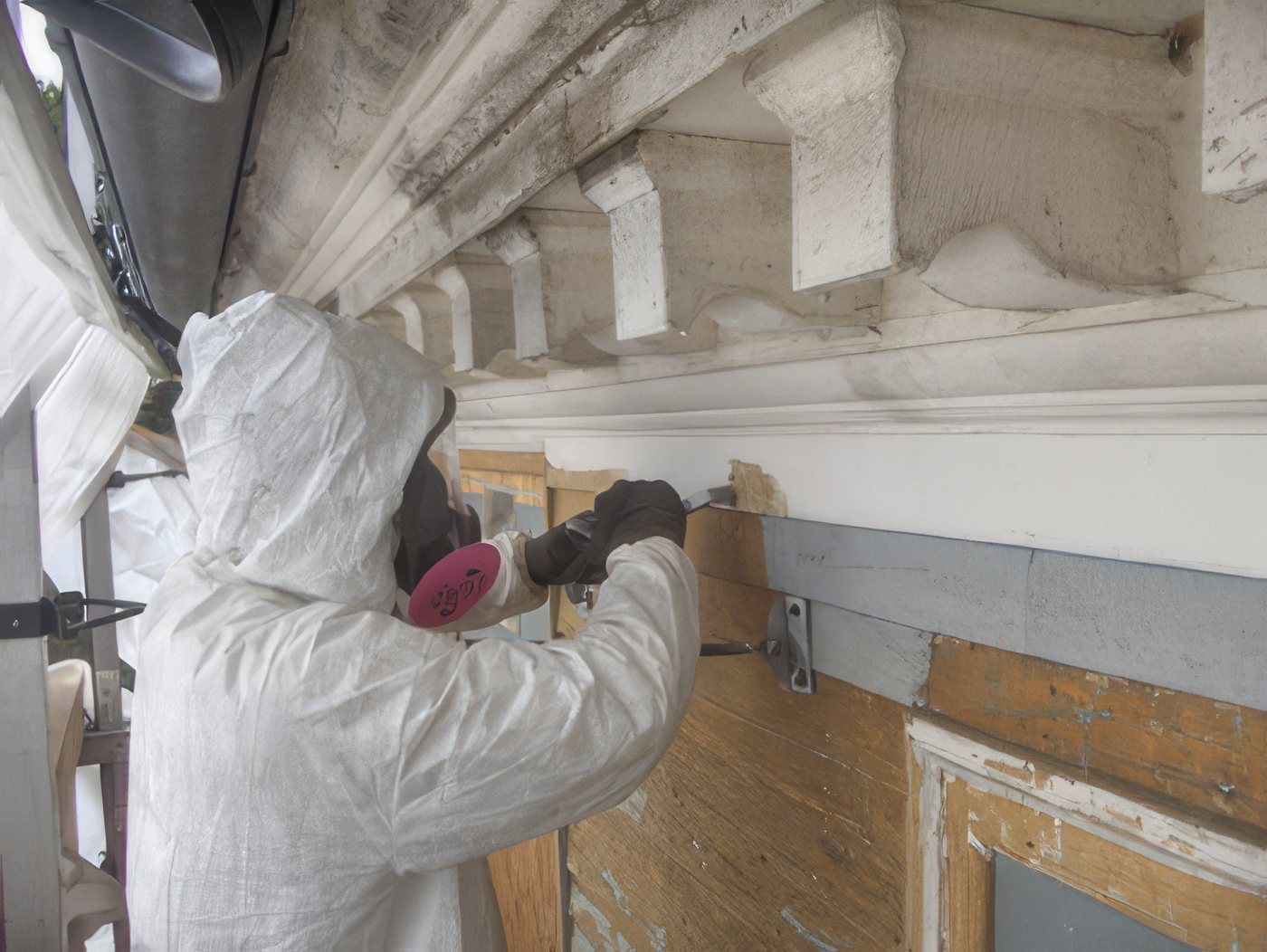 A person wearing protective gear and gloves working on a construction or restoration project, possibly repairing a wooden or plaster surface in a building.
