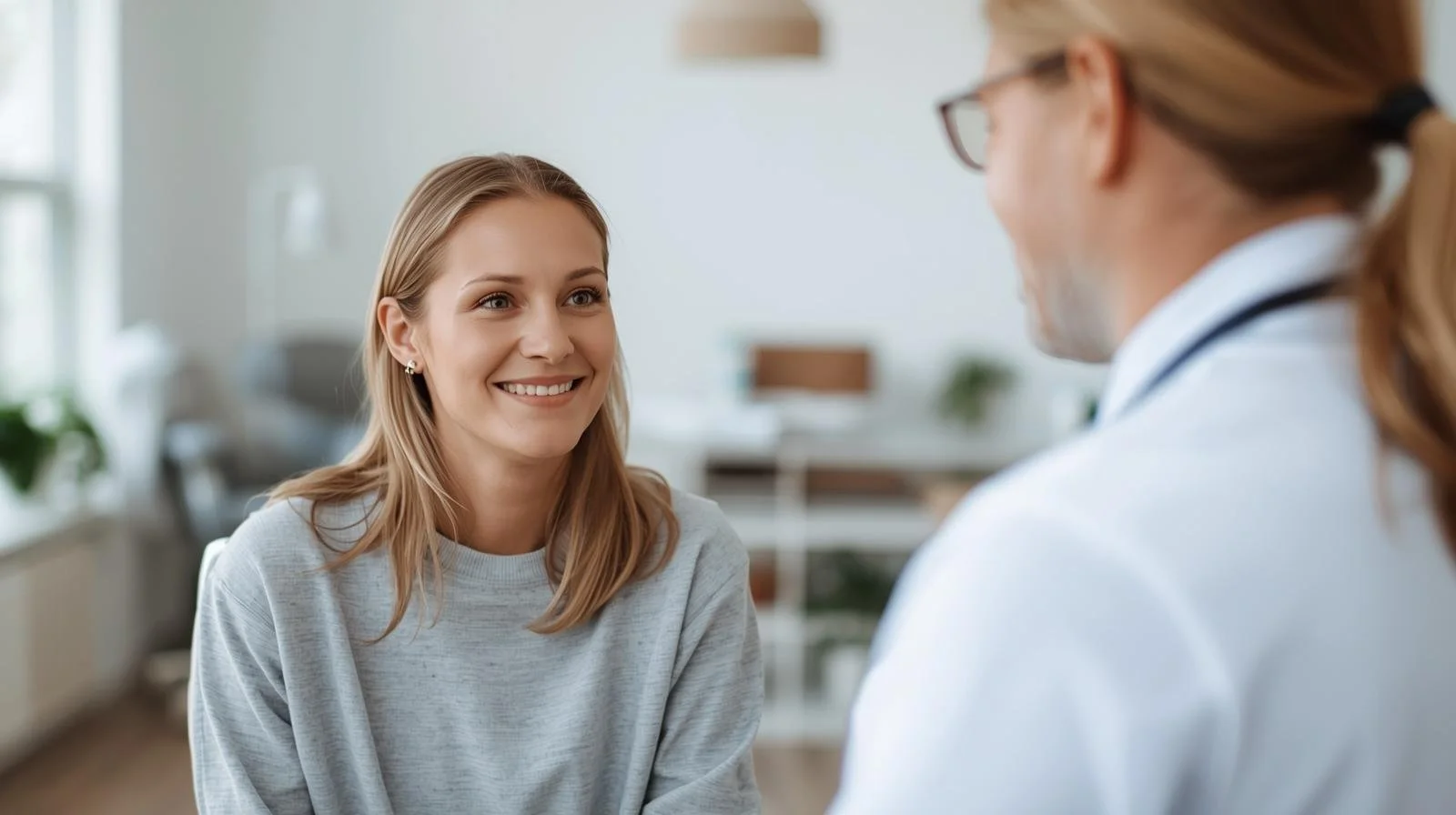 A young woman with blonde hair smiling and talking to a professional doctor or therapist in a well-lit room.