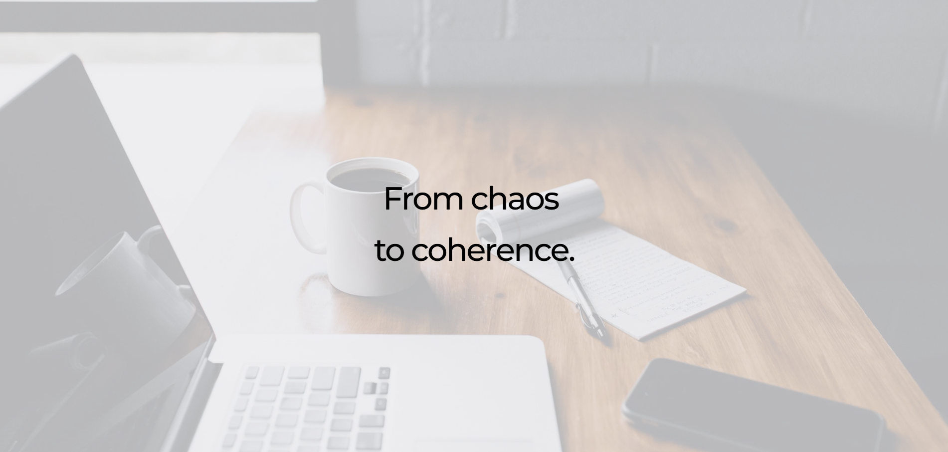 A workspace with a laptop, a cup of coffee, a notepad with a pen, and a smartphone on a wooden table, with a wall in the background; overlaid text reads "From chaos to coherence."