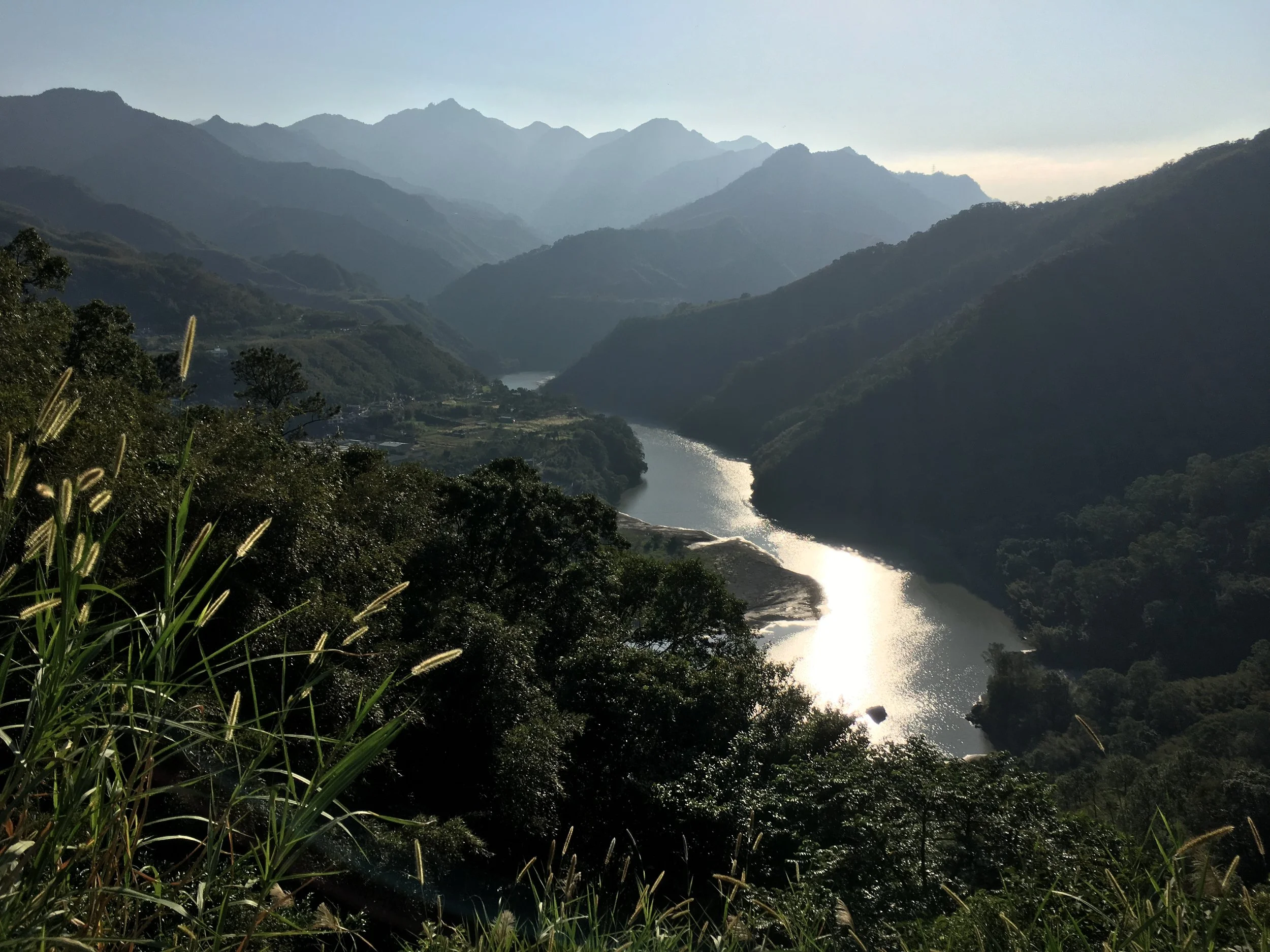 Scenic view of a winding river through lush green mountains with misty peaks in the background, taken during daylight.