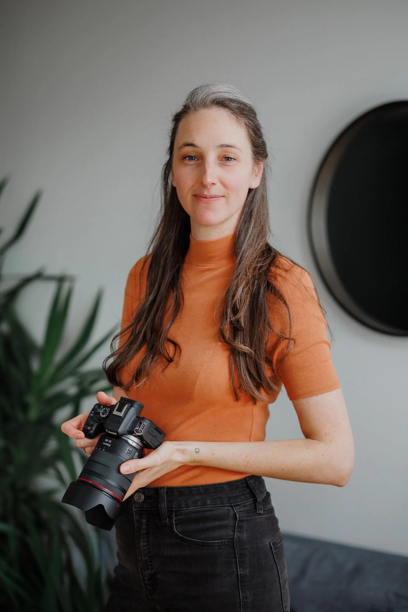 Woman standing with a camera in her hands and a soft smile