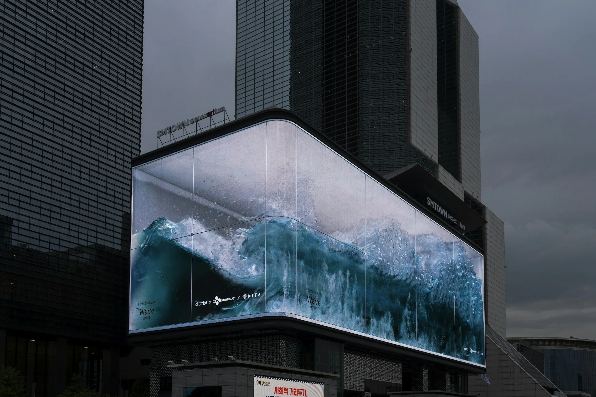 Large electronic billboard displaying an animated image of blue ocean waves on a building in an urban area with skyscrapers.
