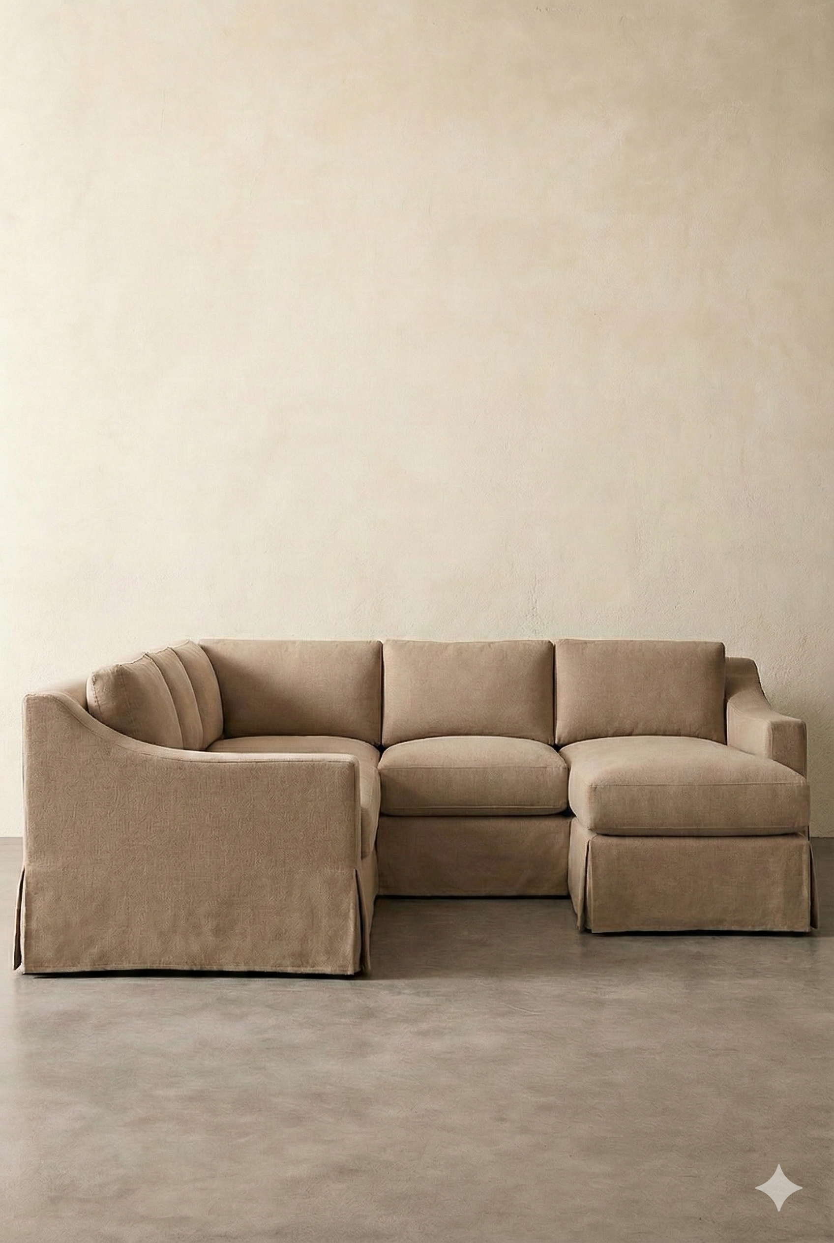 Beige sectional sofa against a plain off-white wall with a concrete floor.