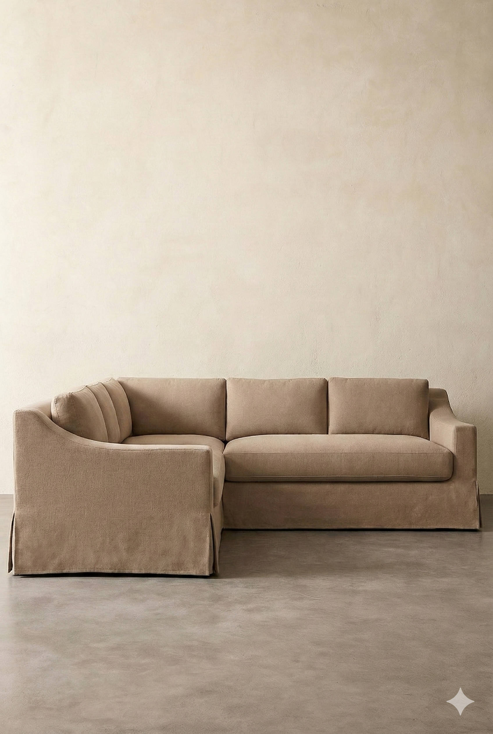 A beige sectional sofa with a curved backrest and plush cushions in a minimalist room with plain beige walls and a gray floor.