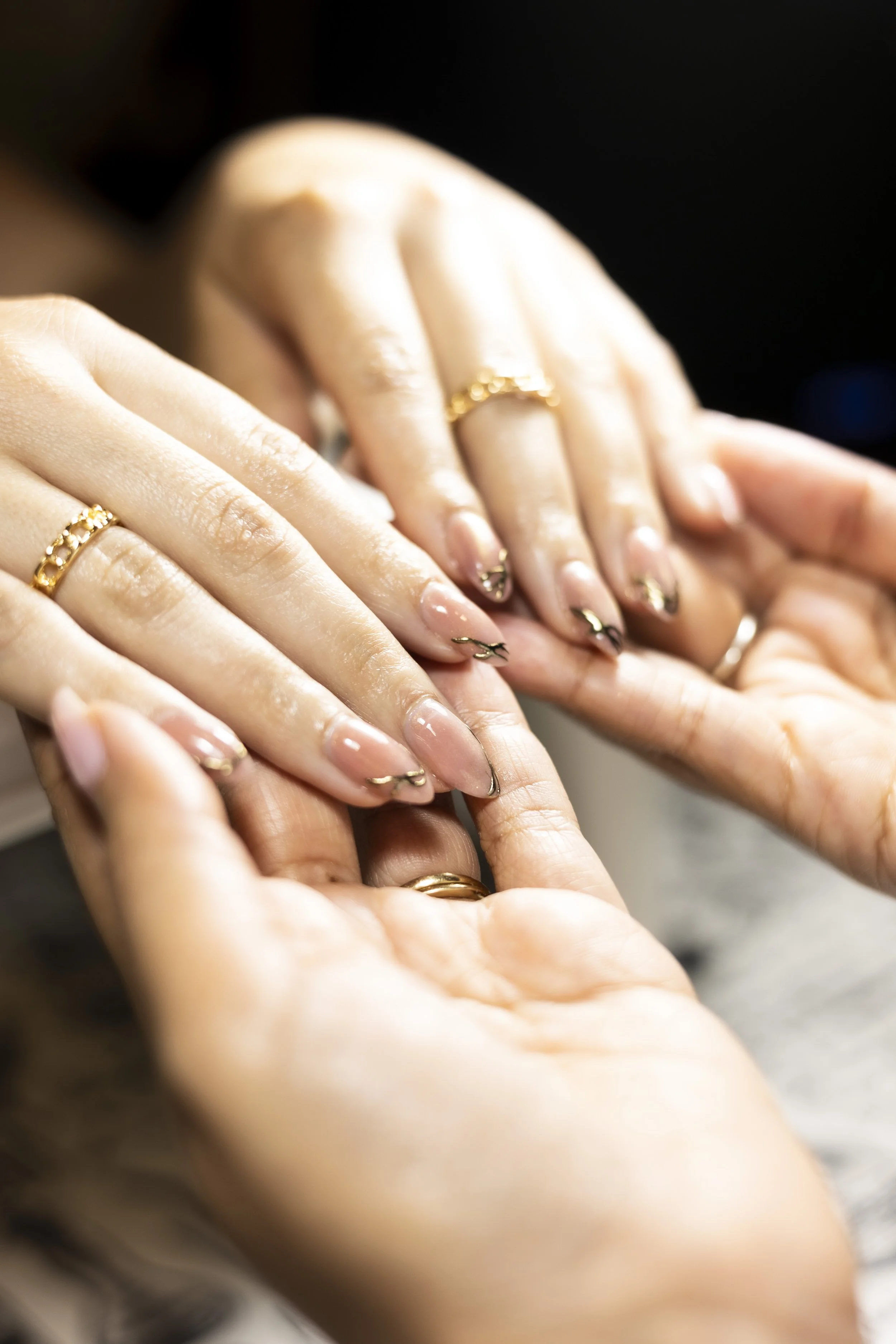 Close-up of hands with manicured nails and gold rings, overlapping each other.