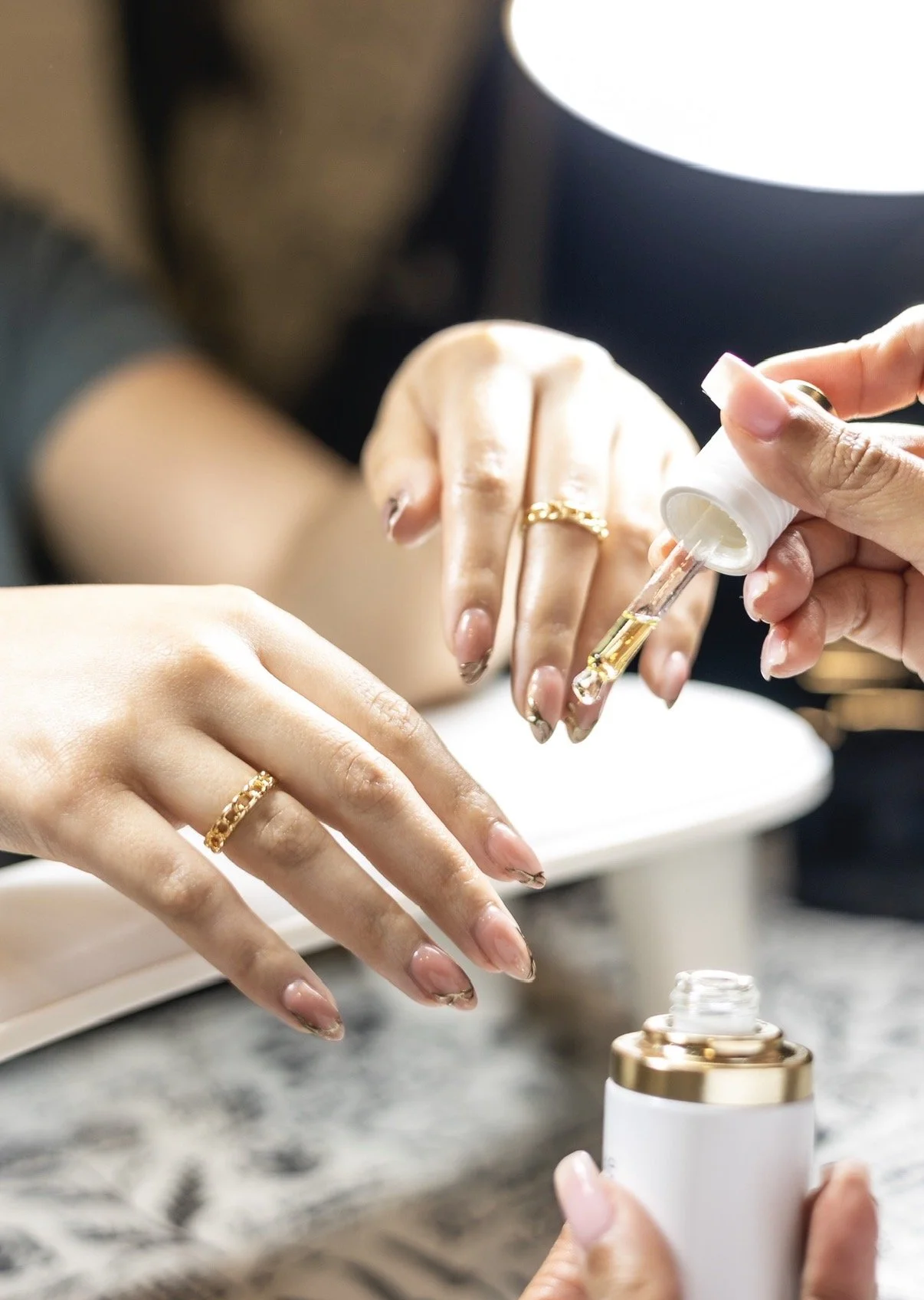 Person applying cuticle oil to nails with a dropper, with hands resting on a table.
