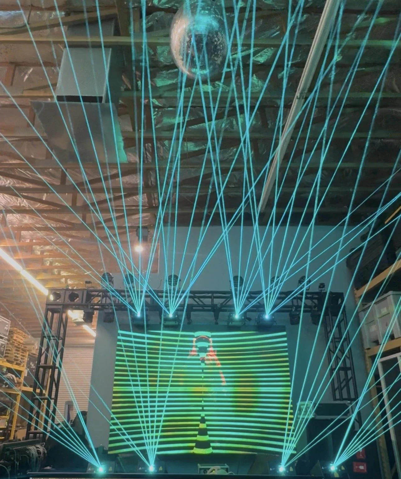 Stage with multiple blue laser light show lasers, a large LED screen, live sound system, trussing setup..