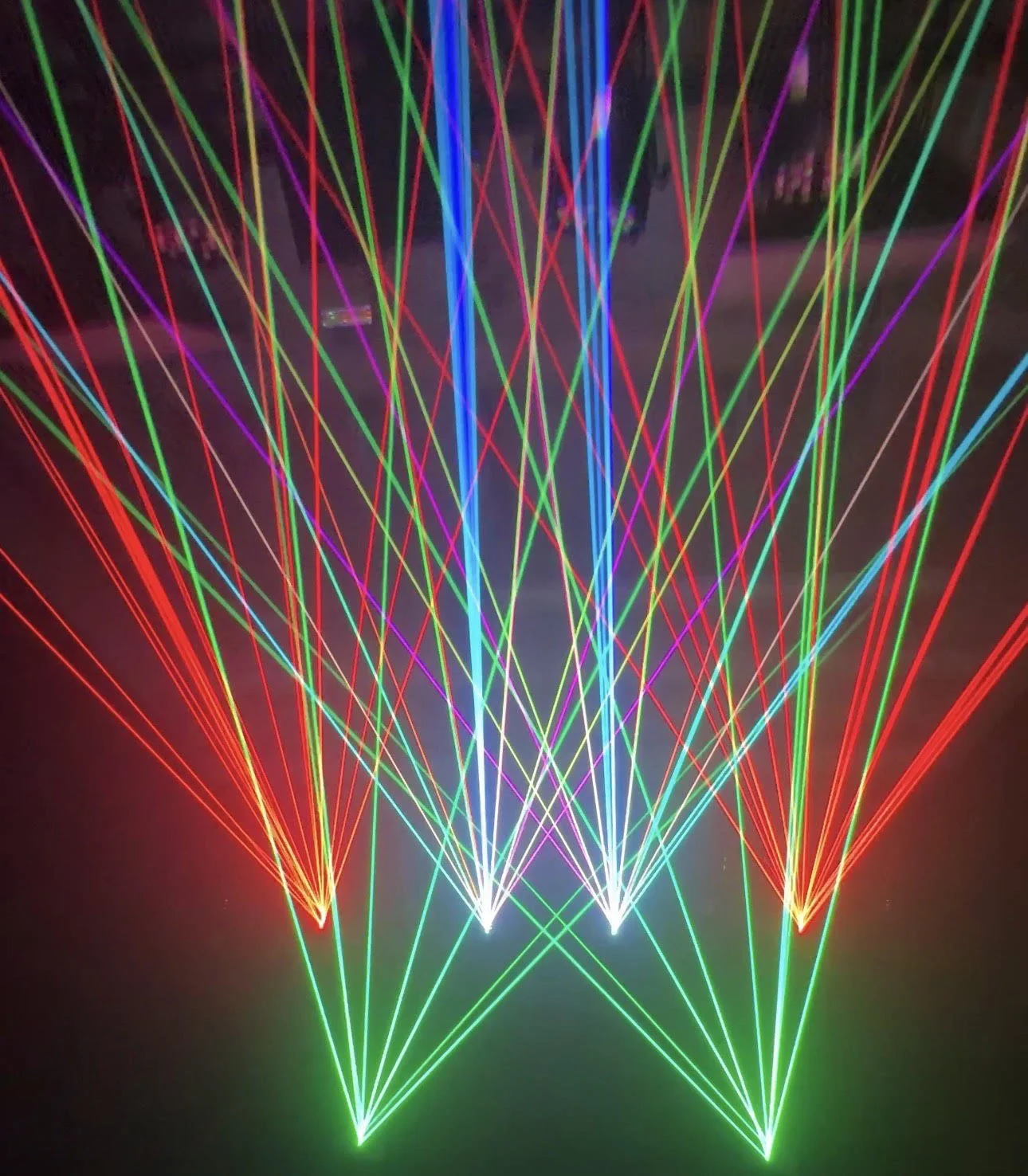 Colorful laser light show beams in red, green, blue, purple, and yellow crossing inside a production studio containing six laser lights.