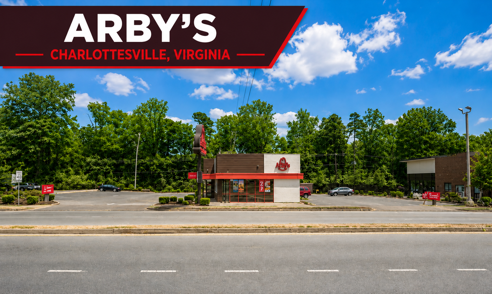 Front view of an Arby's restaurant in Charlottesville, Virginia, with a large sign on the building and a parking lot with a few cars, green trees behind, blue sky with clouds.