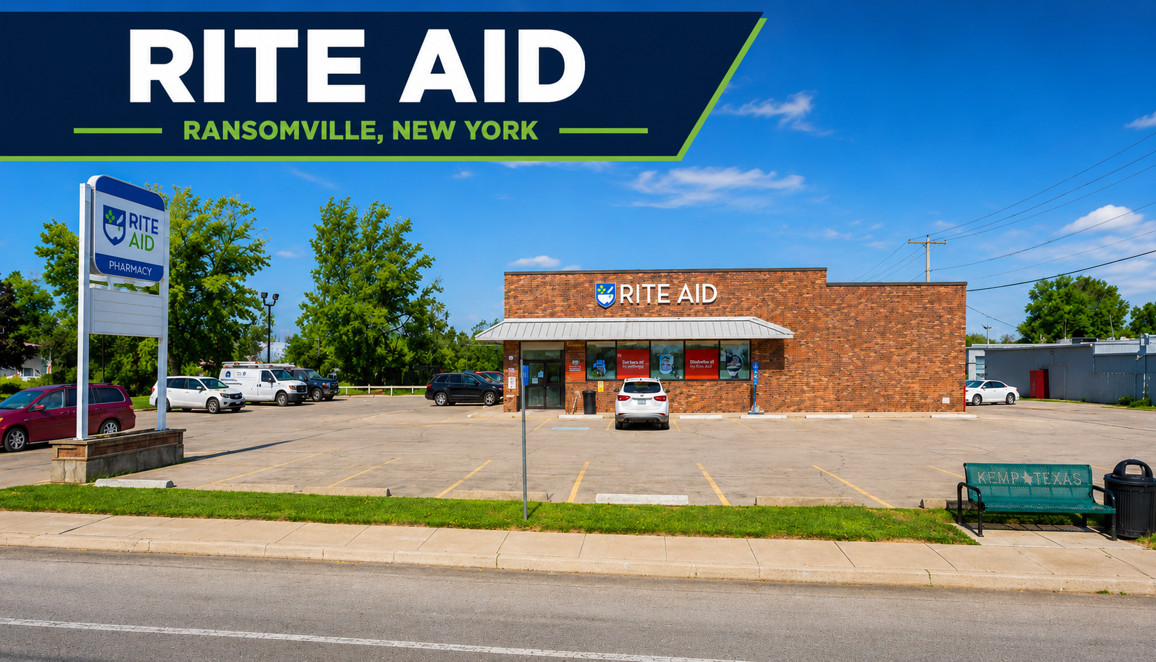 Front view of a Rite Aid pharmacy store with a large parking lot in Ransomville, New York. The store has a brick exterior with a white awning over the entrance and the Rite Aid sign above it. Several cars are parked in the lot, and a sign in the foreground indicates it is a pharmacy. A bench with 'KEMP TEXAS' inscribed on it and a trash can are on the sidewalk.