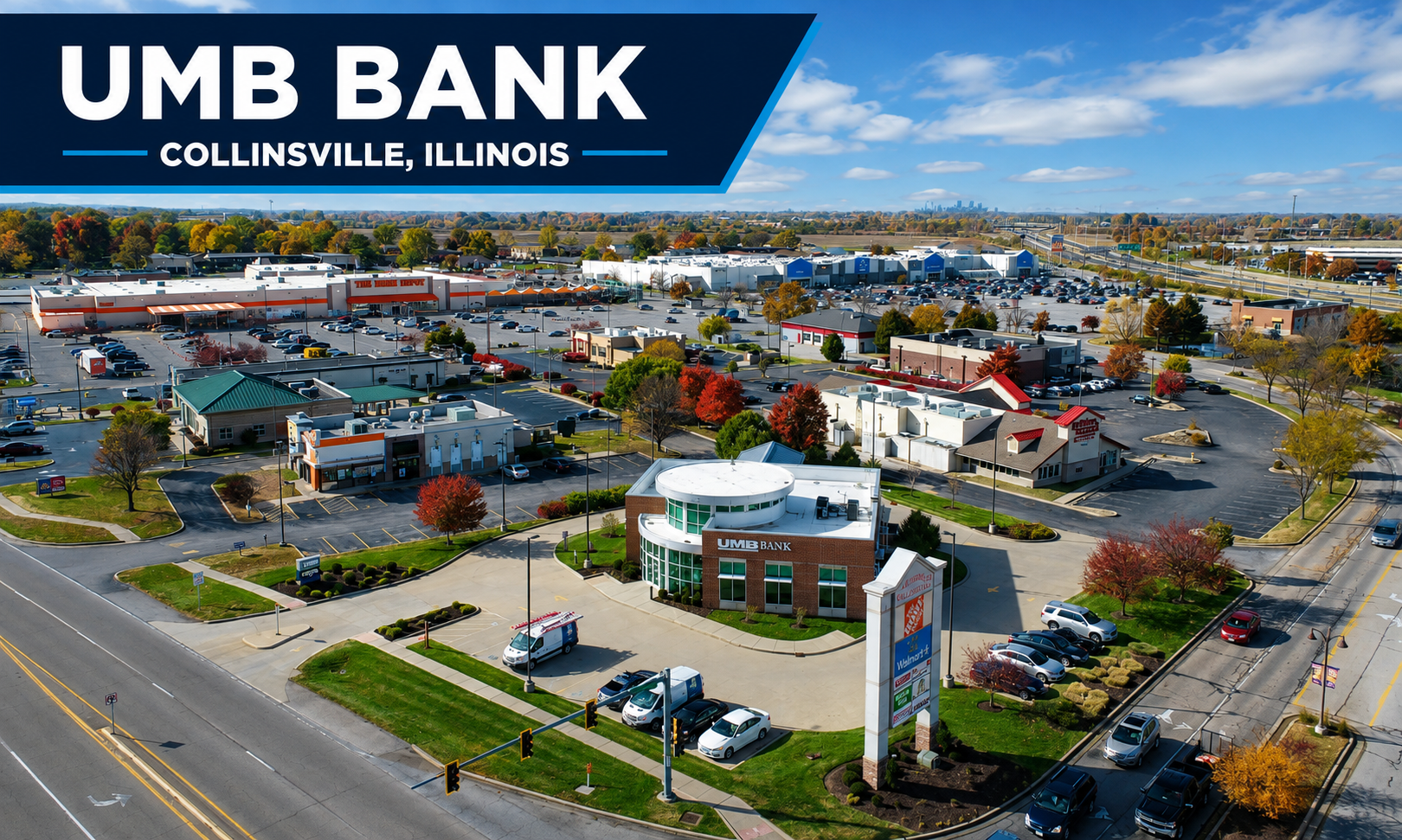 Aerial view of UMB Bank in Collinsville, Illinois, with surrounding shopping centers, parking lots, and trees with fall foliage, under a partly cloudy sky.