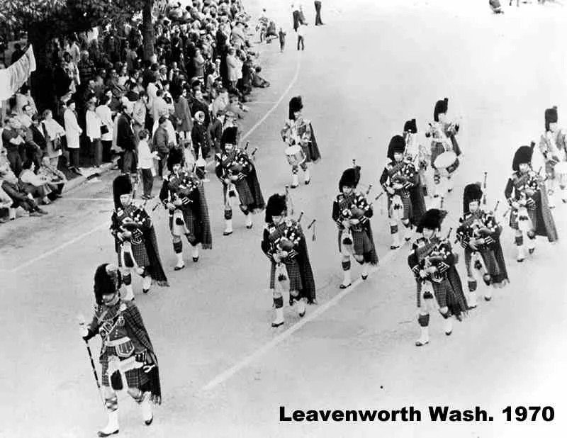 A marching band of bagpipers dressed in traditional Scottish attire performs in a parade at Leavenworth, Washington, in 1970, with spectators lining the street to watch.