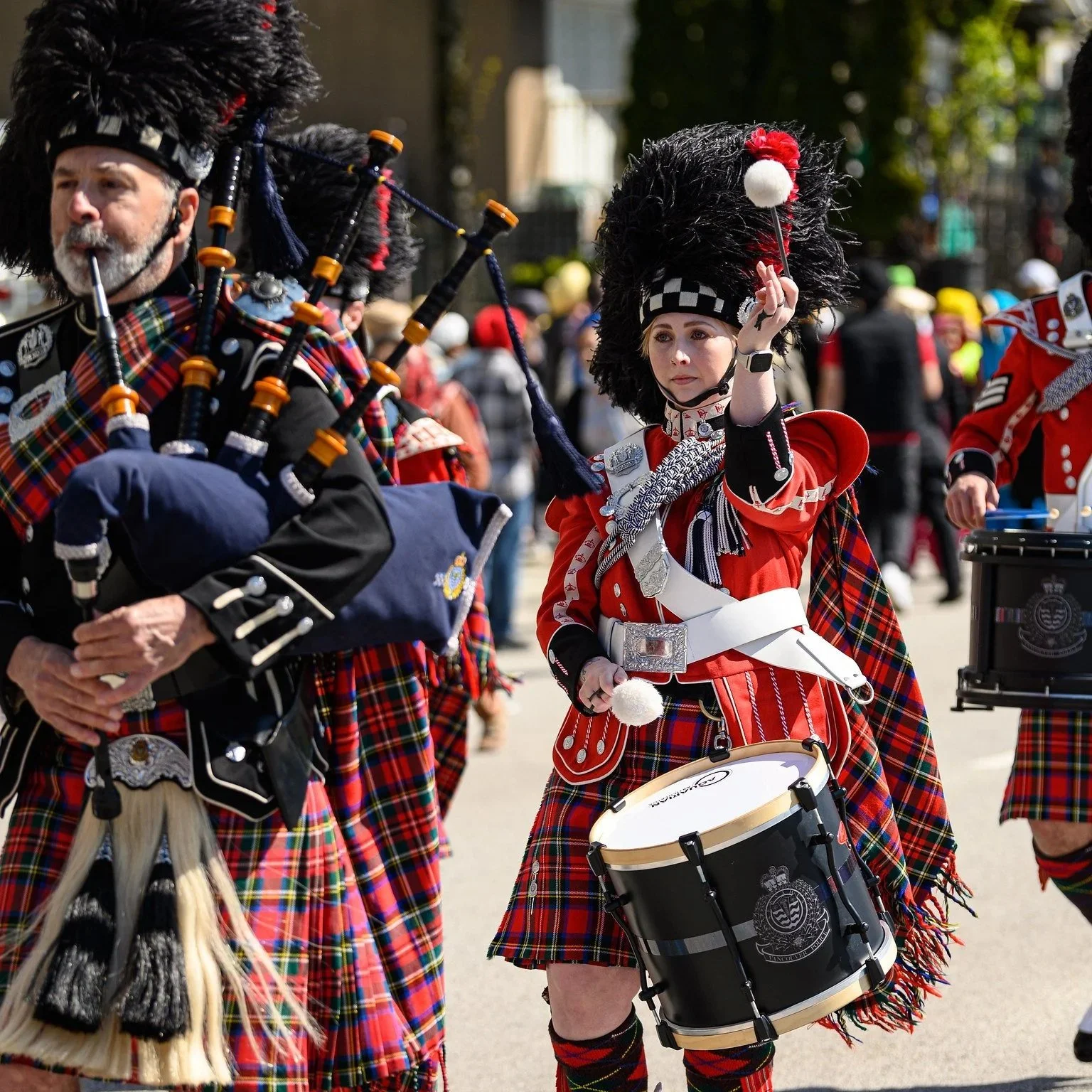 People dressed in traditional Scottish Highland dress, including kilts, playing bagpipes and drums in a parade or celebration.