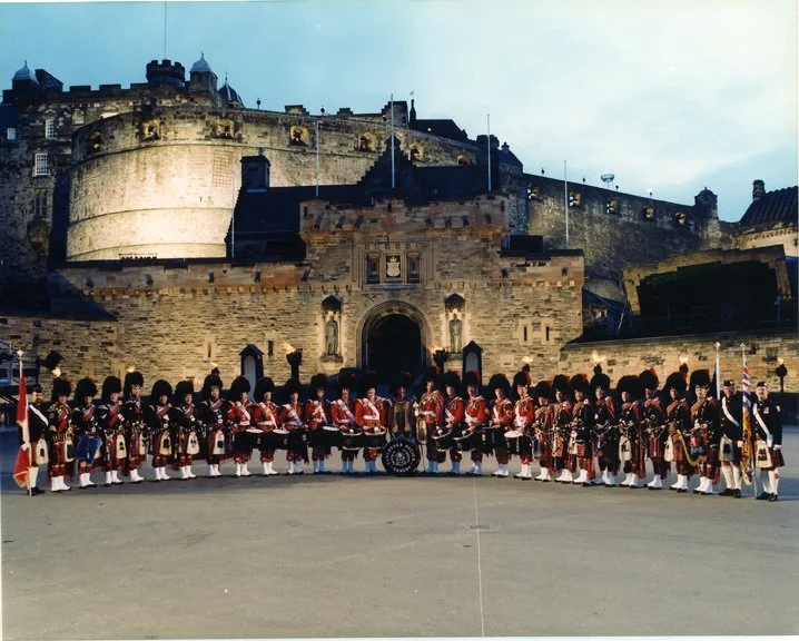 Scottish soldiers in traditional uniforms standing in front of a historic stone fortress.