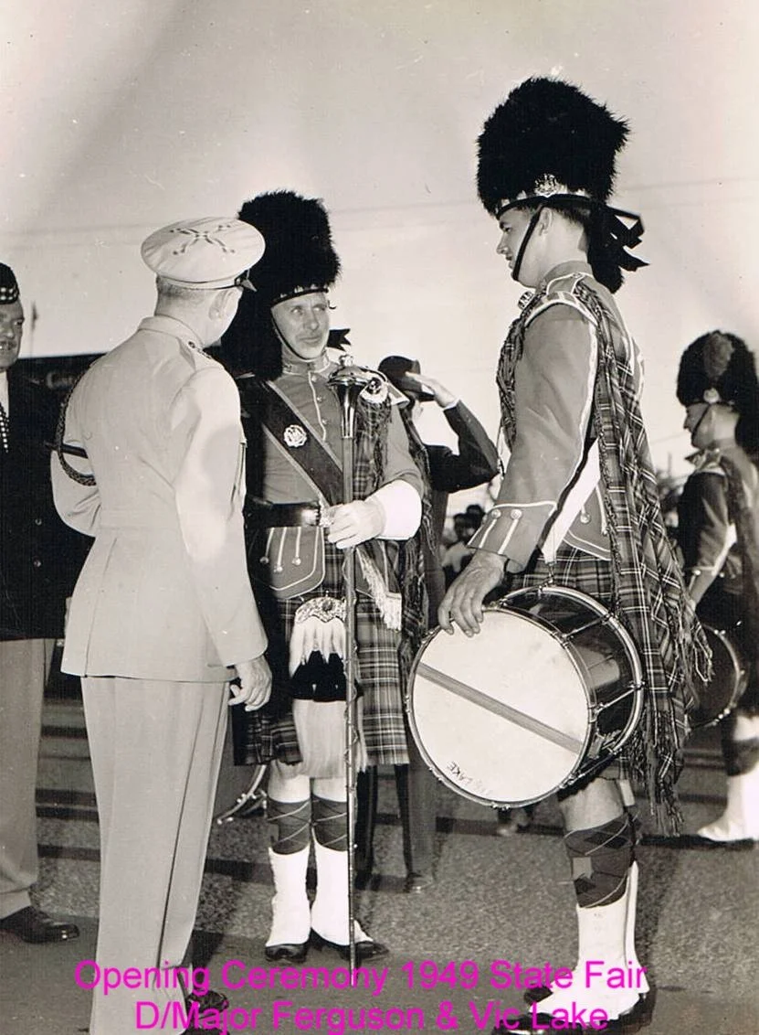 Black and white photo of men in Scottish Highland dress, including kilts, sporrans, and tall feathered hats, at the 1949 State Fair opening ceremony, with a woman in uniform in the background.