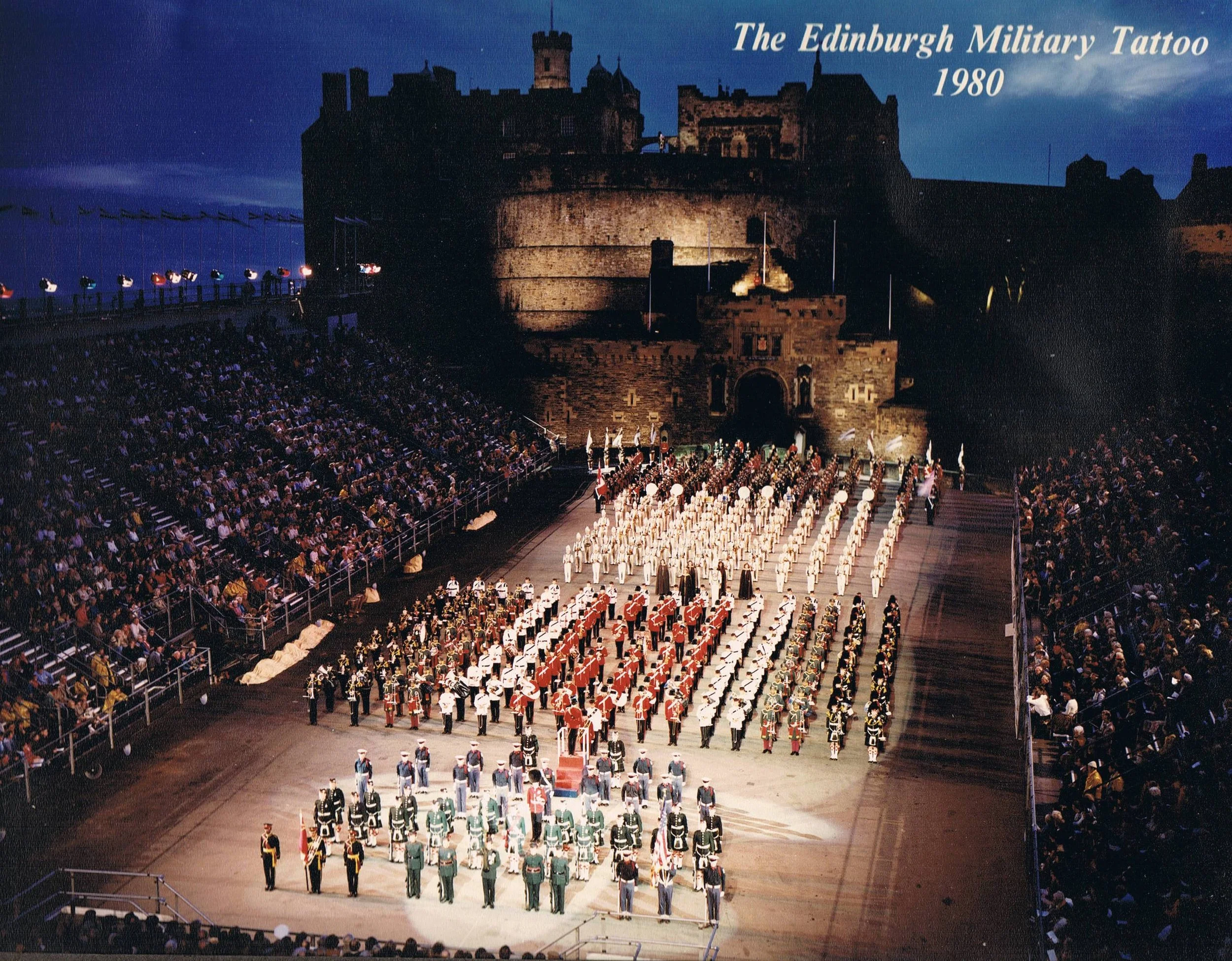 Nighttime outdoor military parade at Edinburgh Castle in 1980, with soldiers in uniform, an audience in the stands, and the castle illuminated in the background.
