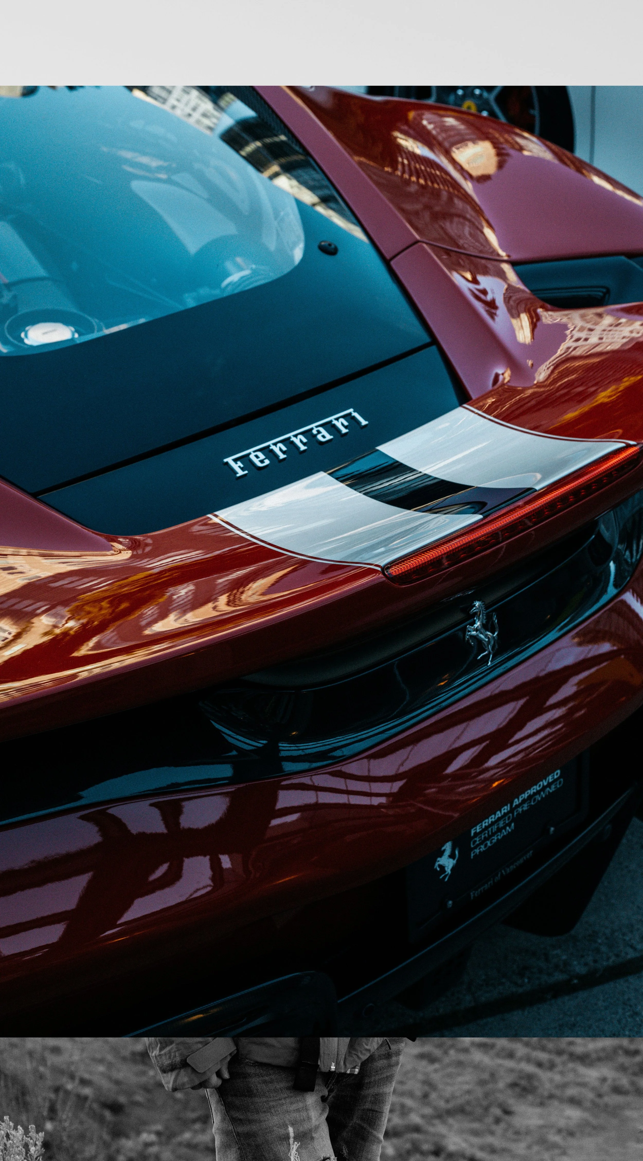 Close-up of a red Ferrari sports car's rear section, featuring Ferrari branding and a prancing horse emblem, with reflections of nearby buildings on its glossy surface.