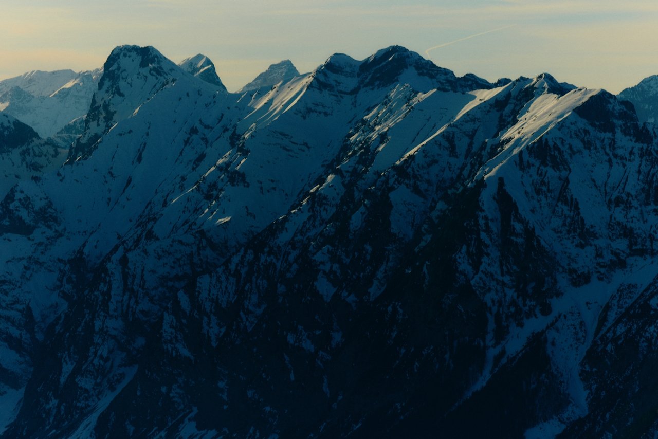 Snow-covered mountain peaks under a pastel-colored sky at sunrise or sunset.