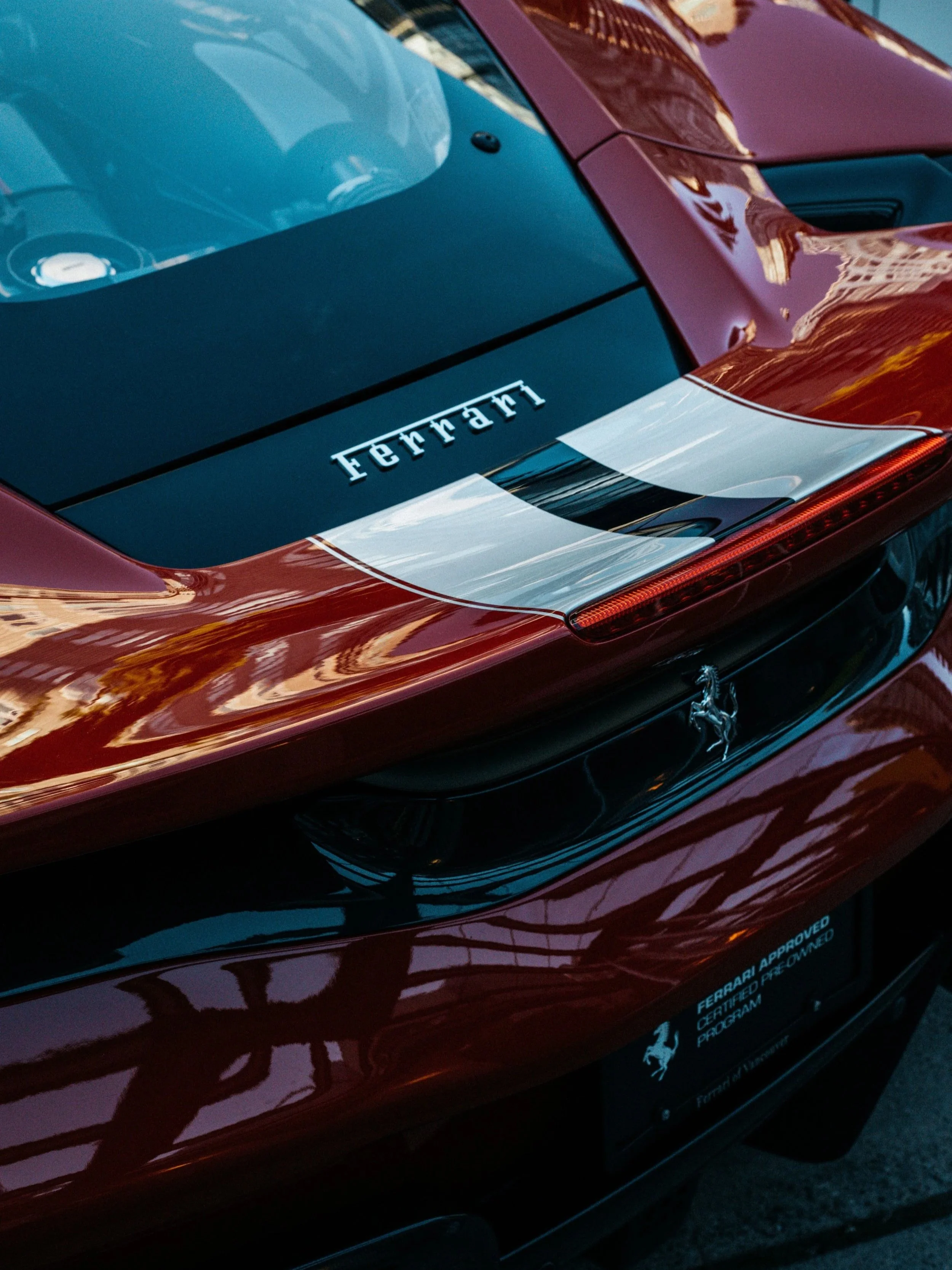 Close-up of the rear of a red Ferrari sports car, showing the Ferrari logo and a black rear window with a white sticker that has the Ferrari name.