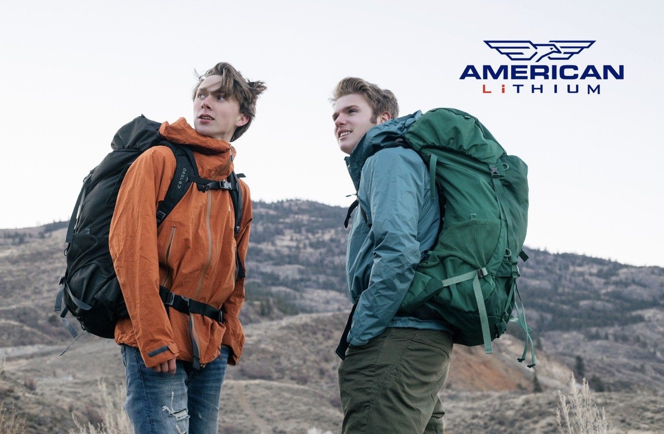 Two young men with backpacks hiking in a mountainous outdoor area.