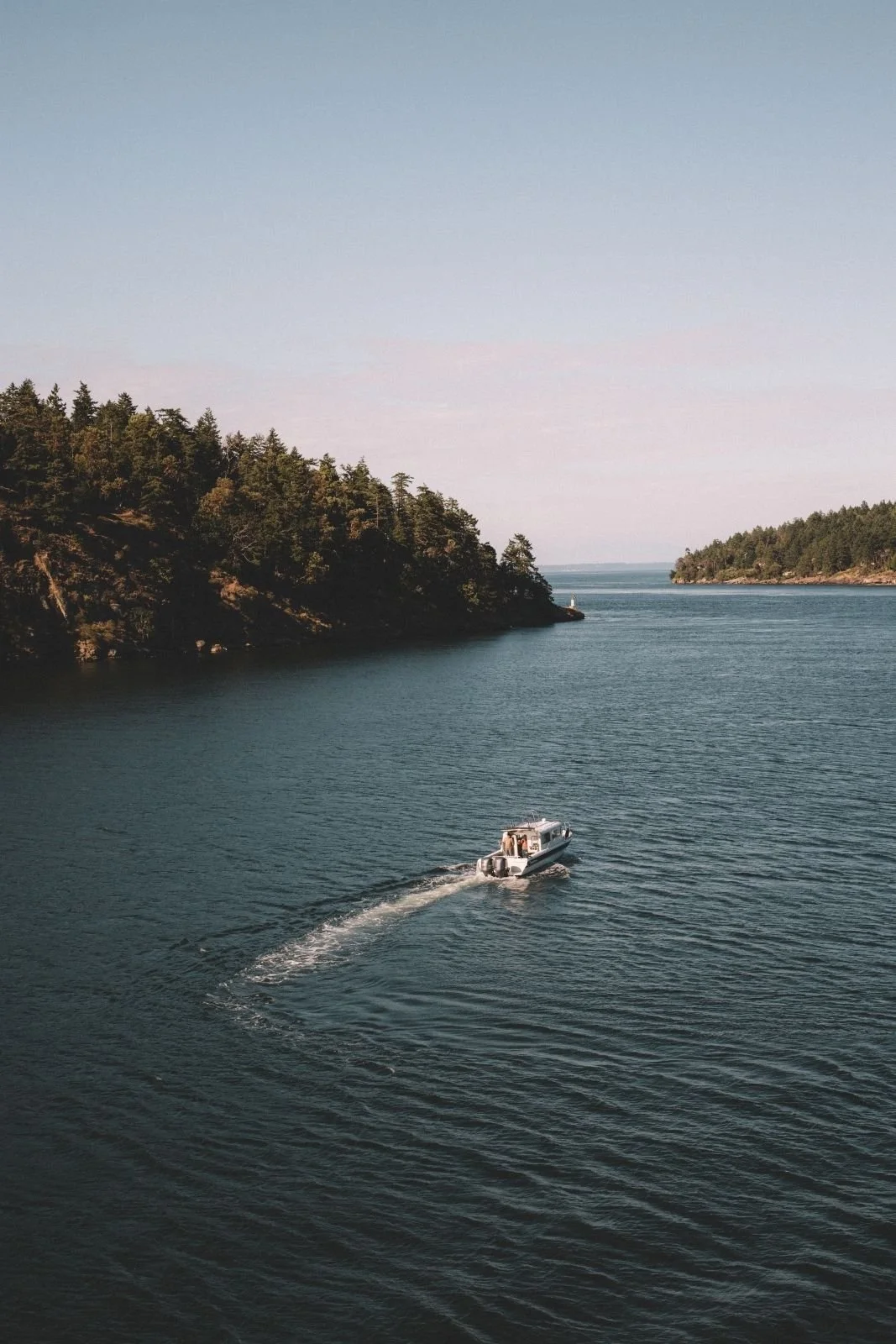 A boat sailing on a calm body of water surrounded by green forested hills under a clear sky.