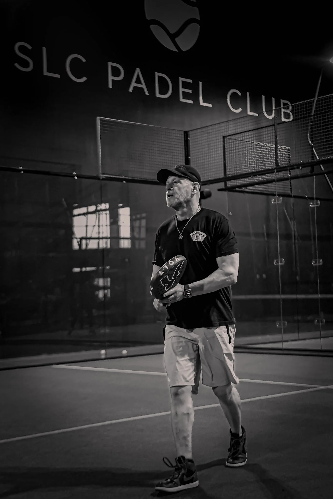 A man playing padel indoors at SLC Padel Club court, wearing sports attire and holding a padel racquet.