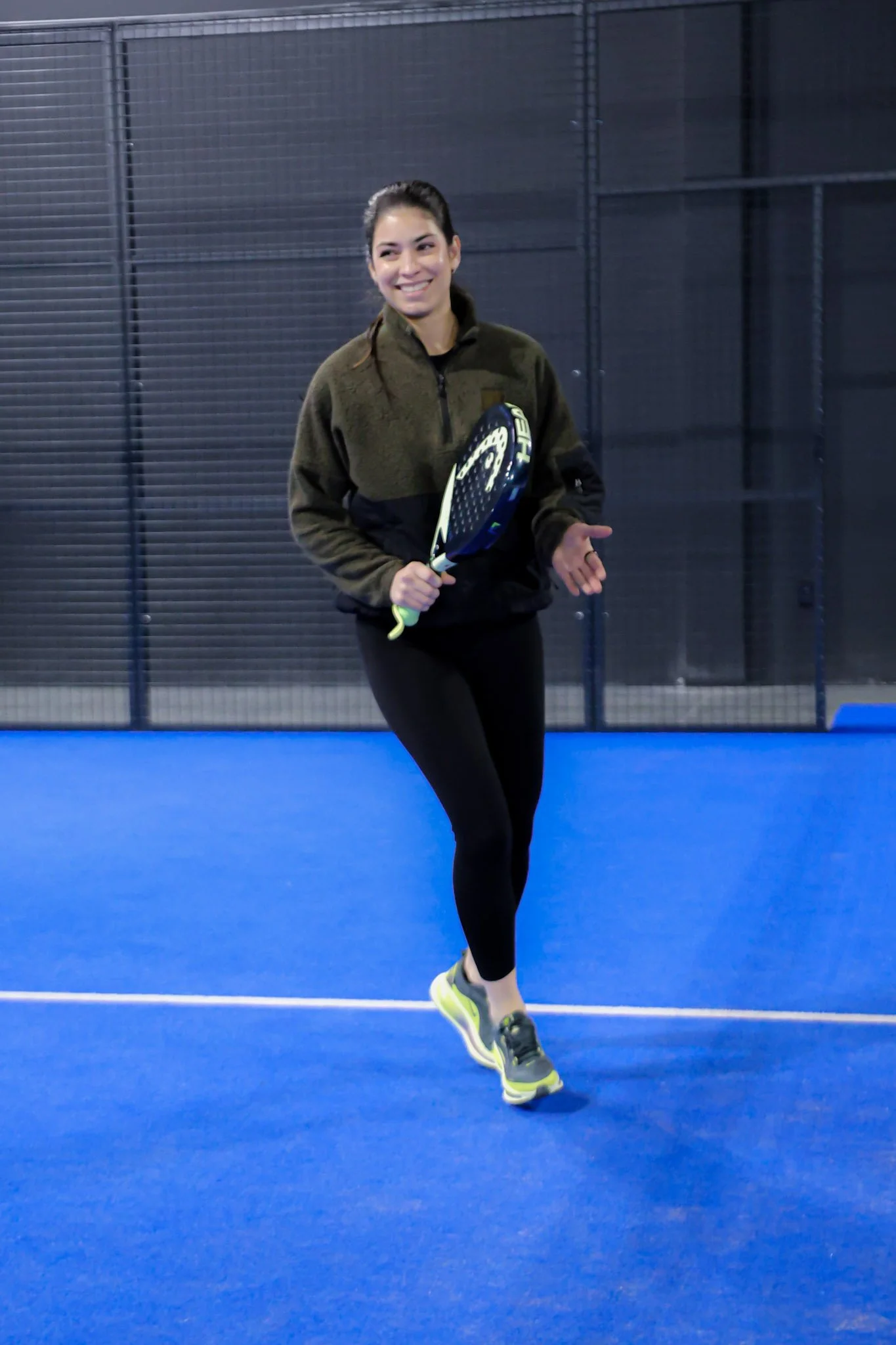Young woman smiling while playing padel indoors on a blue padel court, holding a padel racquet.