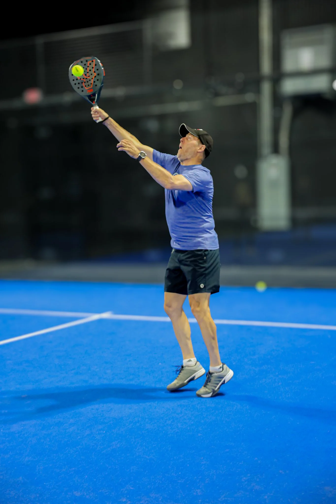 A man playing padel on an indoor padel court, preparing to hit the padel ball with his padel racquet.