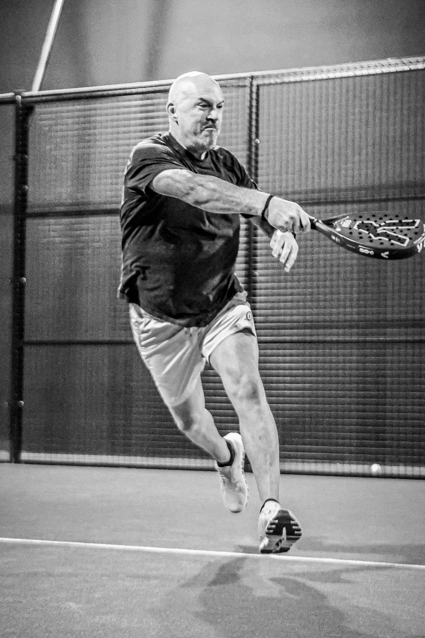 A man playing padel on an indoor padel court, holding a padel racket and hitting a padel ball.