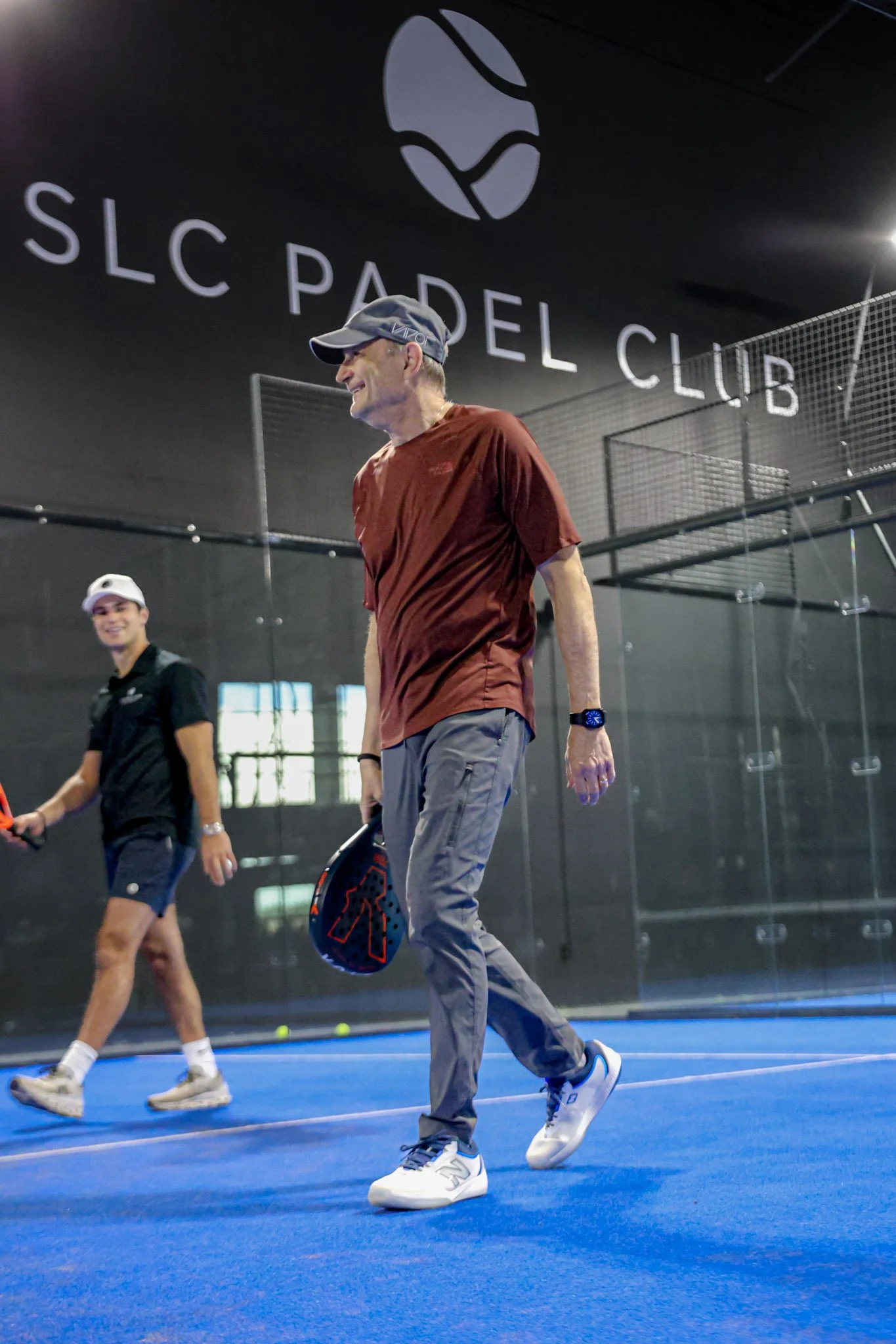 People playing padel on an indoor padel court with the SLC Padel Club logo visible on the wall.