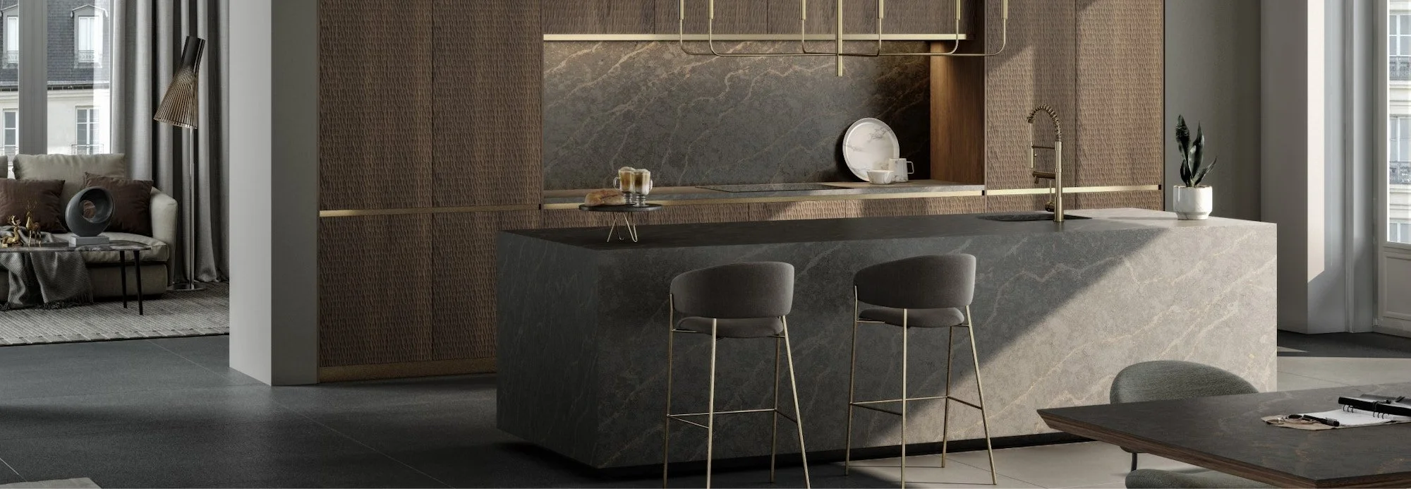 Modern kitchen with a large marble island, two gray bar stools, a sink with a gold faucet, and decorative plates and plants. The background features dark textured wood cabinets and a marble backsplash. Bright natural light floods in from large windows to the right.