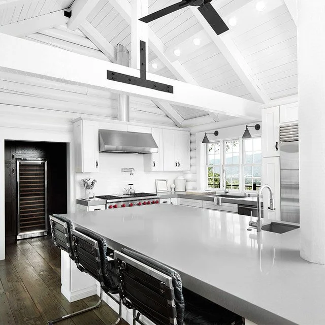 A bright, modern kitchen with white cabinetry, a large white island, stainless steel appliances, and a vaulted ceiling with a ceiling fan.