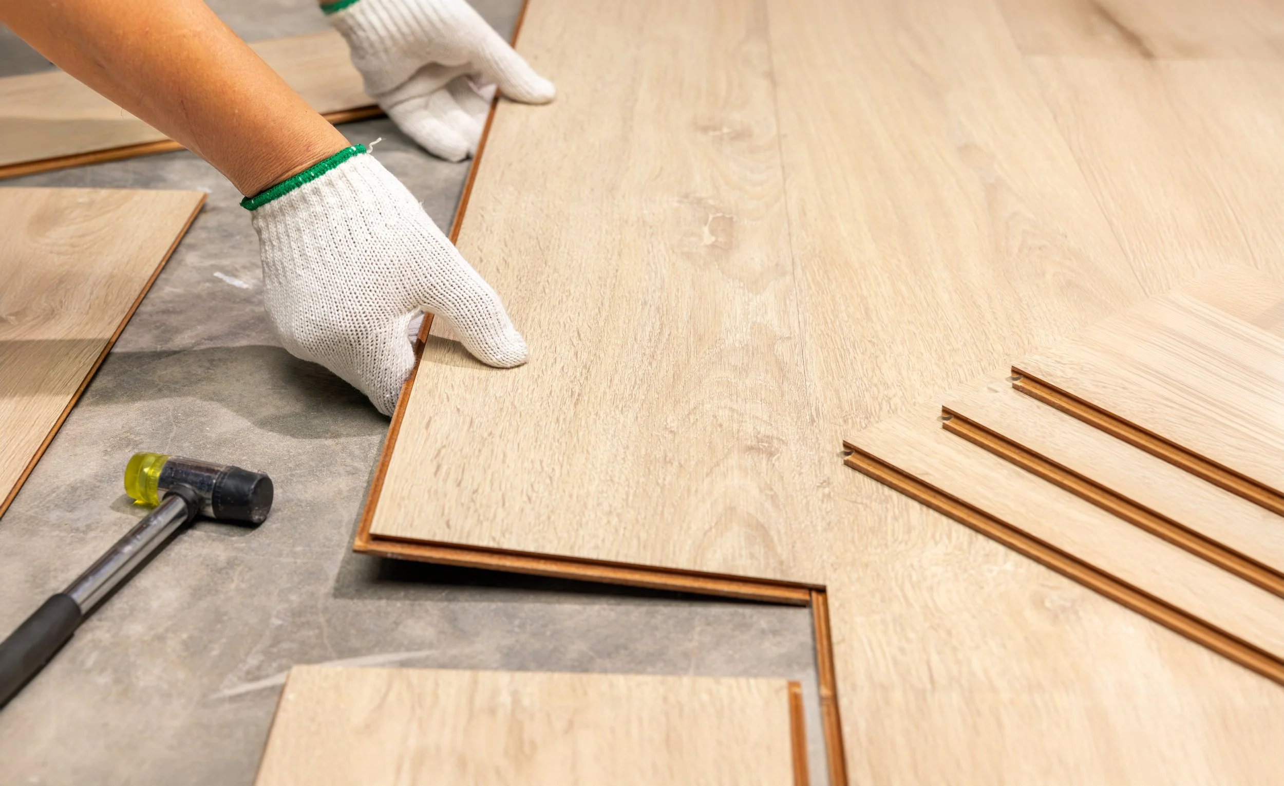 Person installing wooden flooring with gloves, spacer strips, and a mallet.