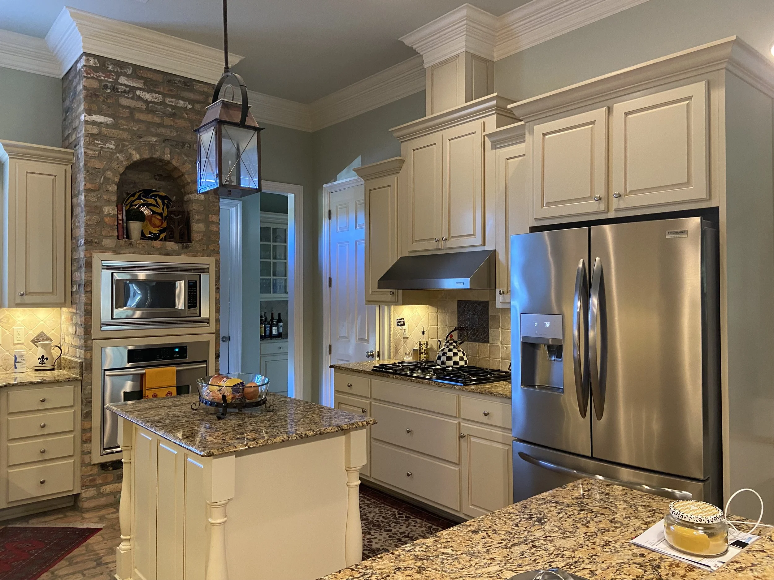 A kitchen with cream-colored cabinets, granite countertops, stainless steel appliances including a refrigerator and a microwave. Canda Construction residential construction and renovation.