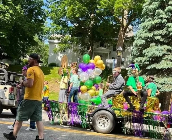 Horn players ride on the back of a parade float. A large group of brightly colored balloons adorn the float.