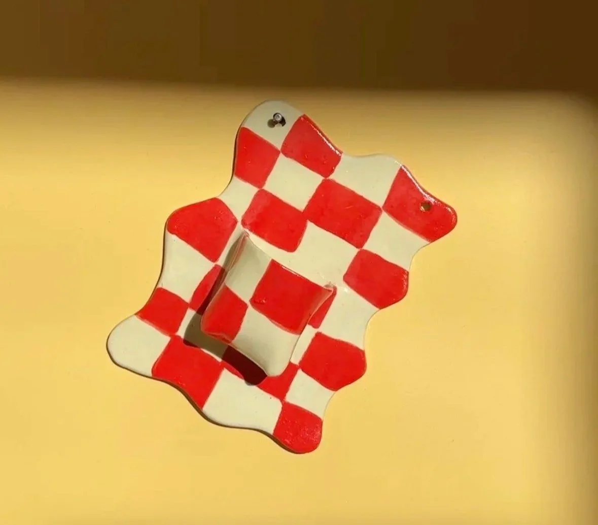 Decorative checkered vase with red and white checkered pattern, mounted on a yellow wall.