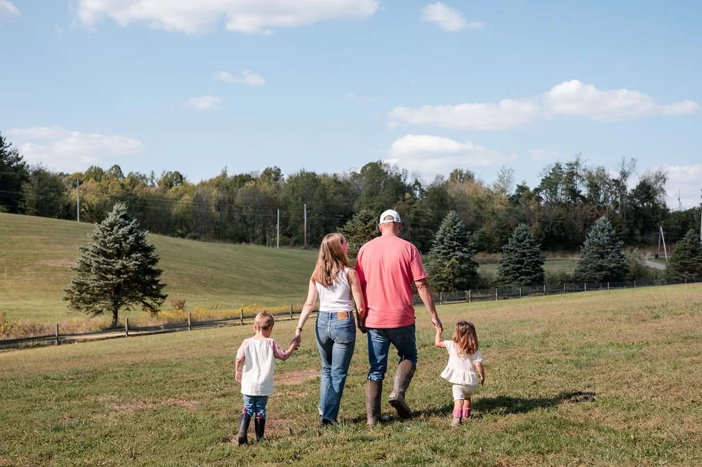 Family walking hand-in-hand across a grassy field on a sunny day.