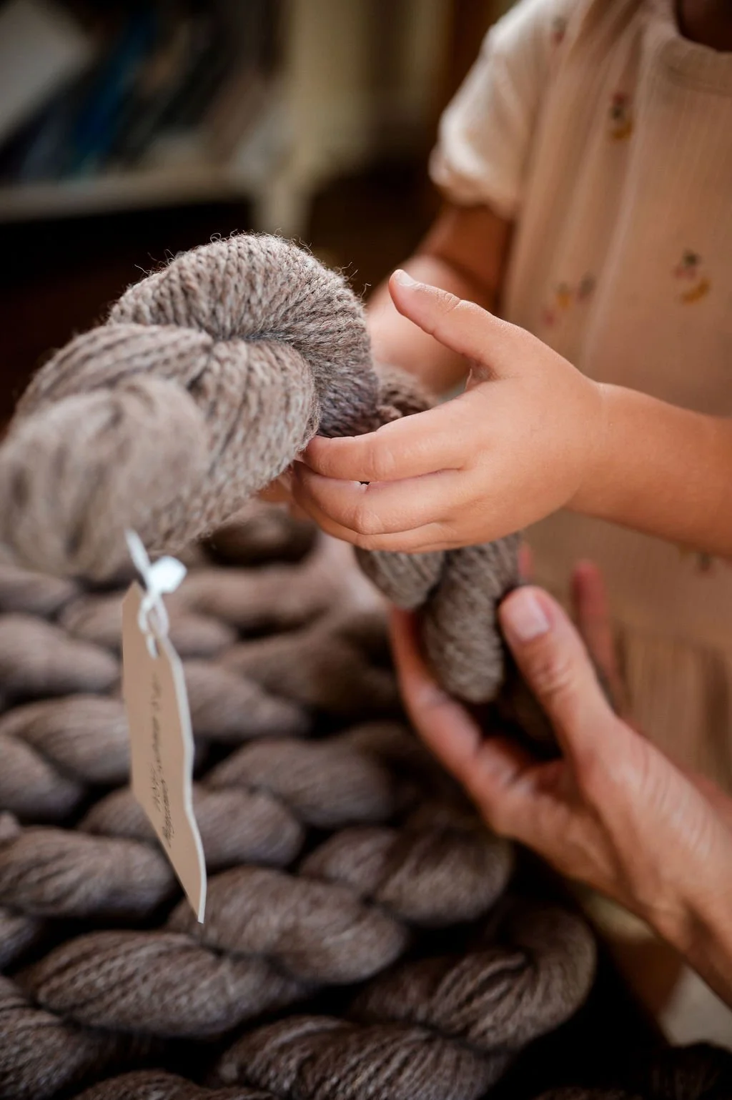 Someone holding an alpaca yarn skein with a large, chunky knitted blanket in the background.